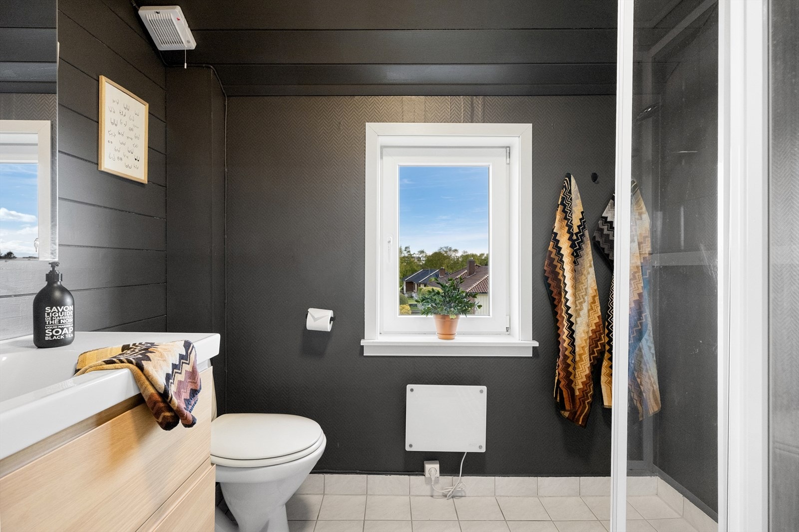 Badet er eldre, med fliser på gulv. Innredet med servant i baderomsmøbel, toalett og dusjhjørne. Galleribilde
