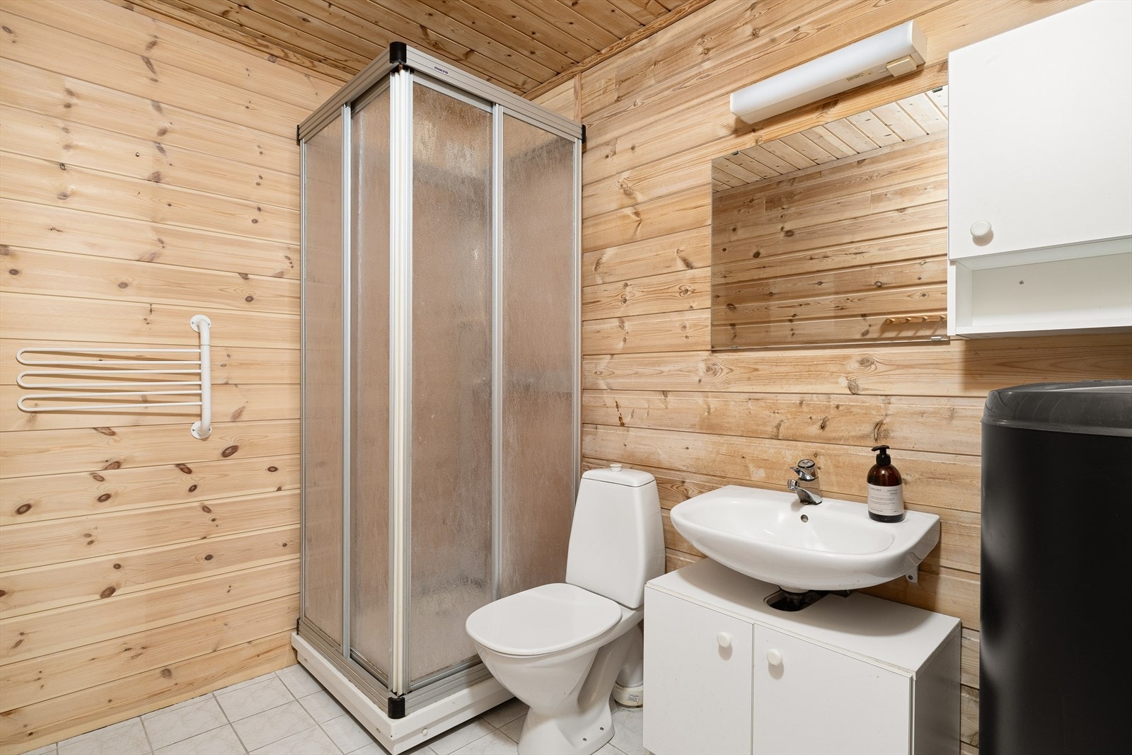 Badet i kjelleren har fliser på gulv med varmekabler og er innredet med dusjkabinett, toalett, servant og varmtvannsbereder. Galleribilde