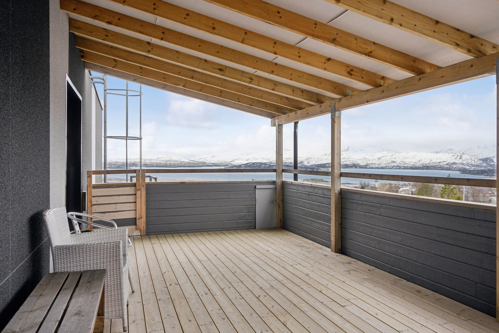 En overbygget, felles uteplass med utsikt mot sjøen og fjellene. Galleribilde