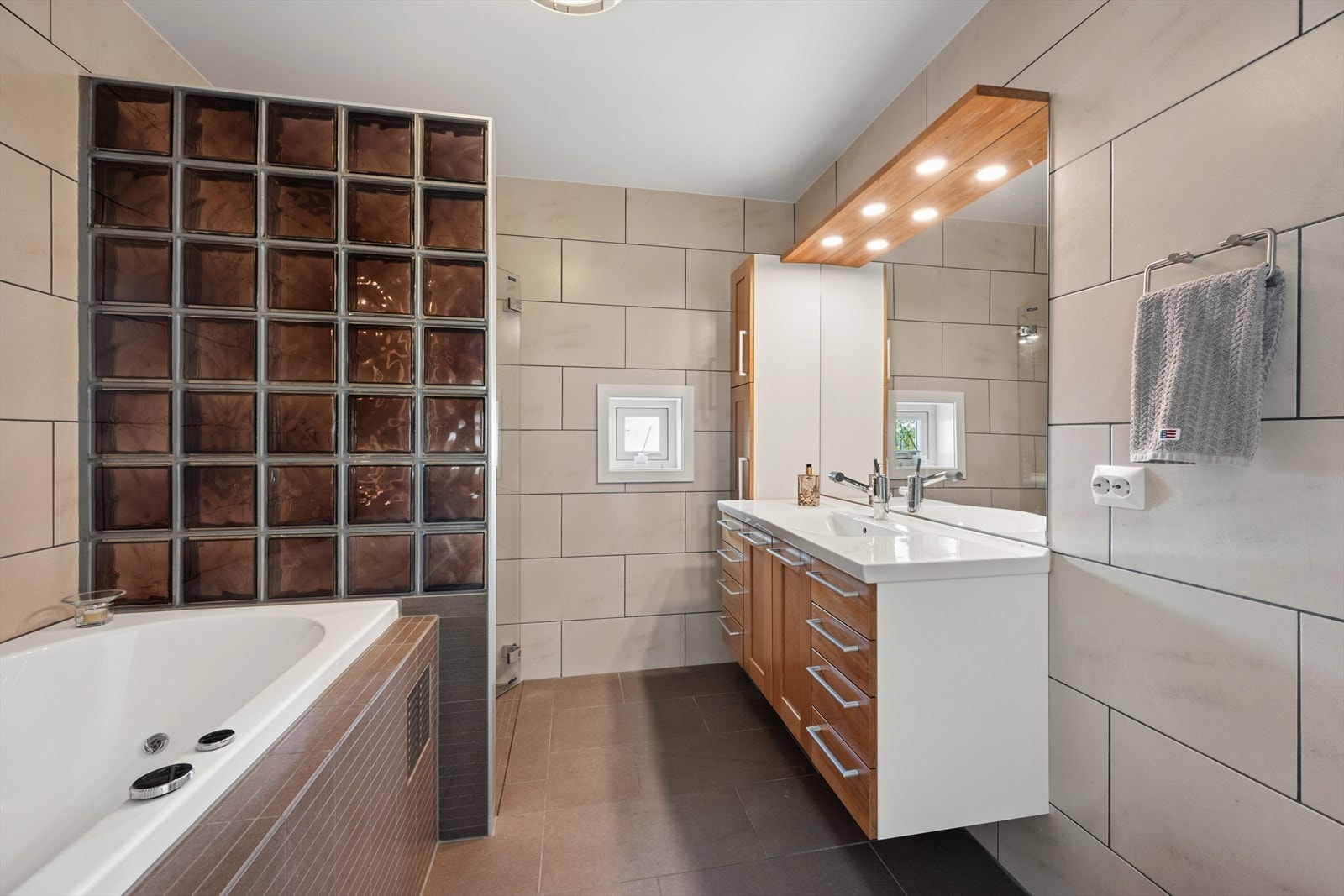 Badet er innredet med en kombinasjon av brune og beige fliser på gulv og vegger. I gulvet har man også varmekabler for ekstra komfort. Galleribilde