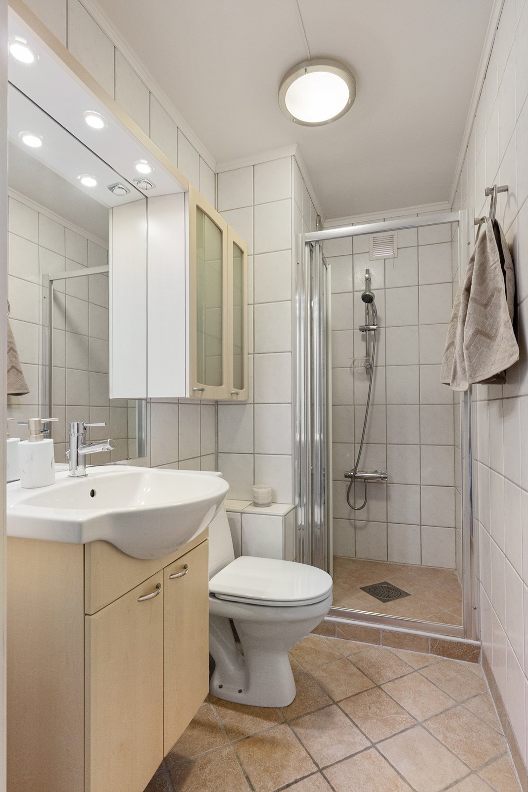 Baderom II har fliser på gulv og vegger og malt himling. Det er montert varmekabler. Badet har gulvmontert toalett, servant med servantskap, speil og to veggskap. Det er praktisk dusjnisje. Galleribilde
