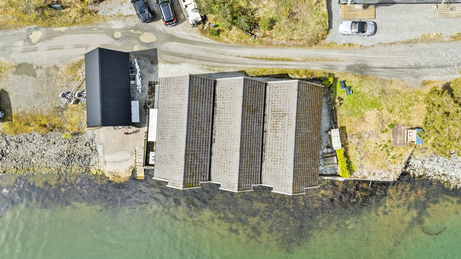 Eigedommen sett frå lufta, med rekkehuset og naustet plassert langs strandlinja. Galleribilde