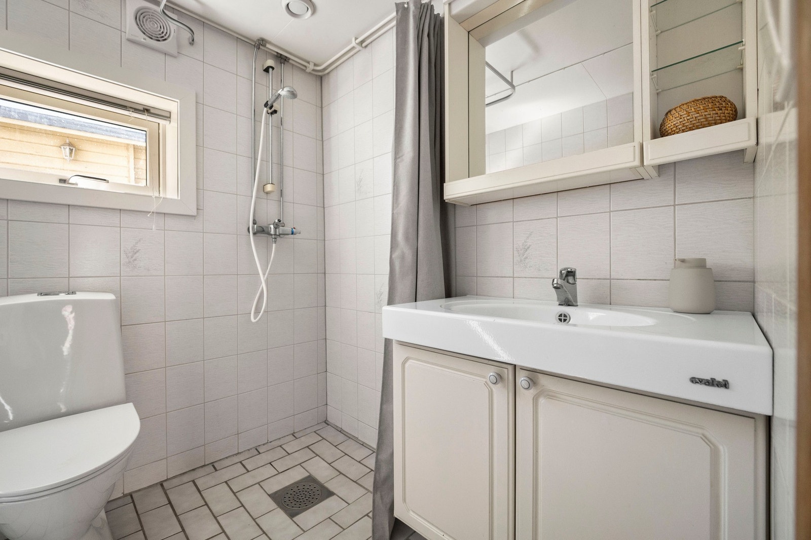 Badet er innredet med servantinnredning med servant, speil med overlys, dusjhjørne med vegghengt dusjarmatur, samt gulvstående toalett. Galleribilde