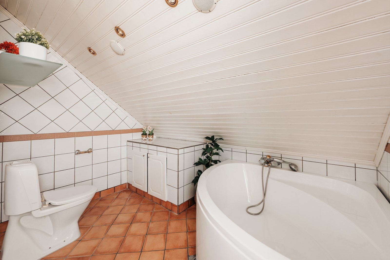 Badet er innredet med hjørnebadekar, toalett og dobbeltservant på underskap. Galleribilde