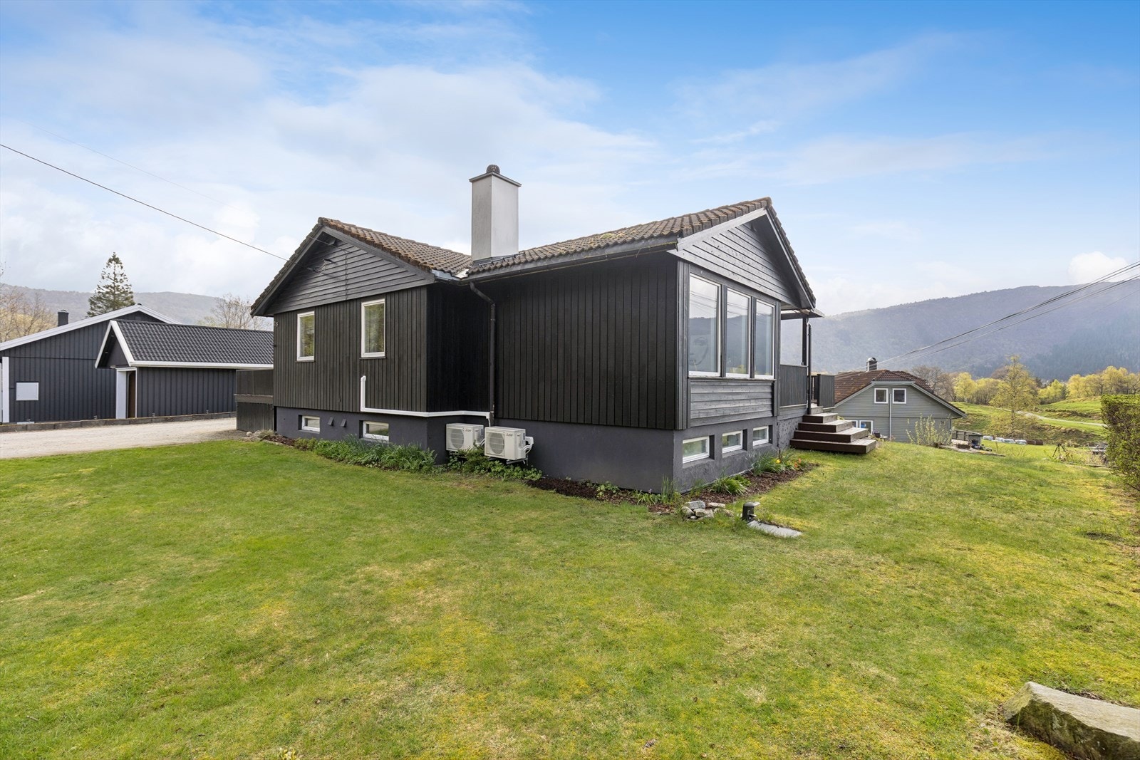 Huset ligger fint til på tomten med plenarealer og naturtomt som fundament på fjell. Galleribilde