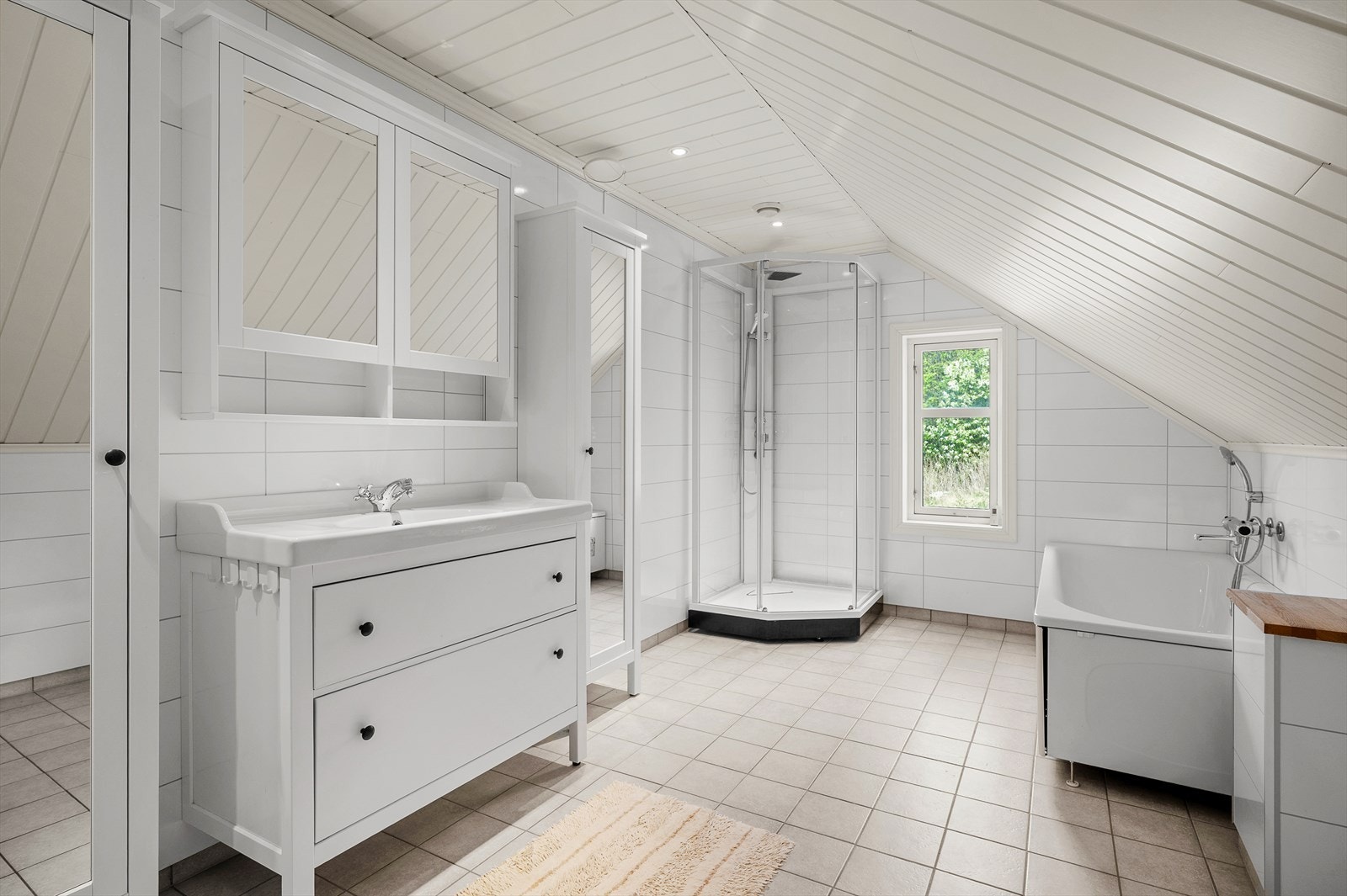 Lyst og flislagt bad med dusjkabinett, badekar og servant i skap. Badet nyter godt av den gode størrelsen på 10m². Galleribilde