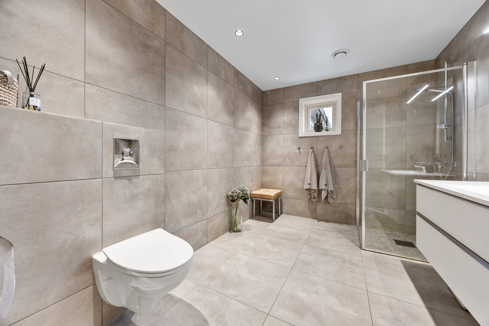 Badet er utstyrt med stilrent servantmøblement, speil med toppmontert belysning, vegghengt toalett samt separat dusjsone. Galleribilde