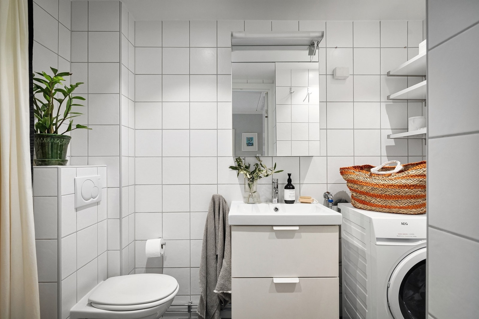 Badet er utstyrt med vegghengt toalett og heldekkende servant med skuffeinnredning under og speilskap med overlys på vegg Galleribilde