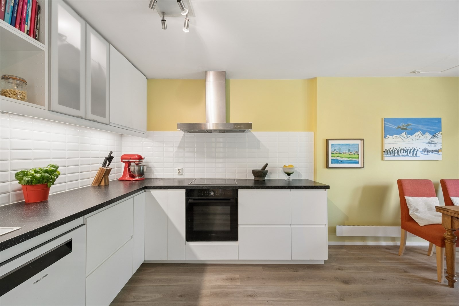 Kjøkkeninnredning fra IKEA med slette lakkerte fronter, laminat benkeplate med fliser på bakvegg, rustfri oppvaskkum, innfelte hvitevarer bestående av stekeovn og platetopp samt frittstående oppvaskmaskin og kombinert kjøle- og fryseskap Galleribilde