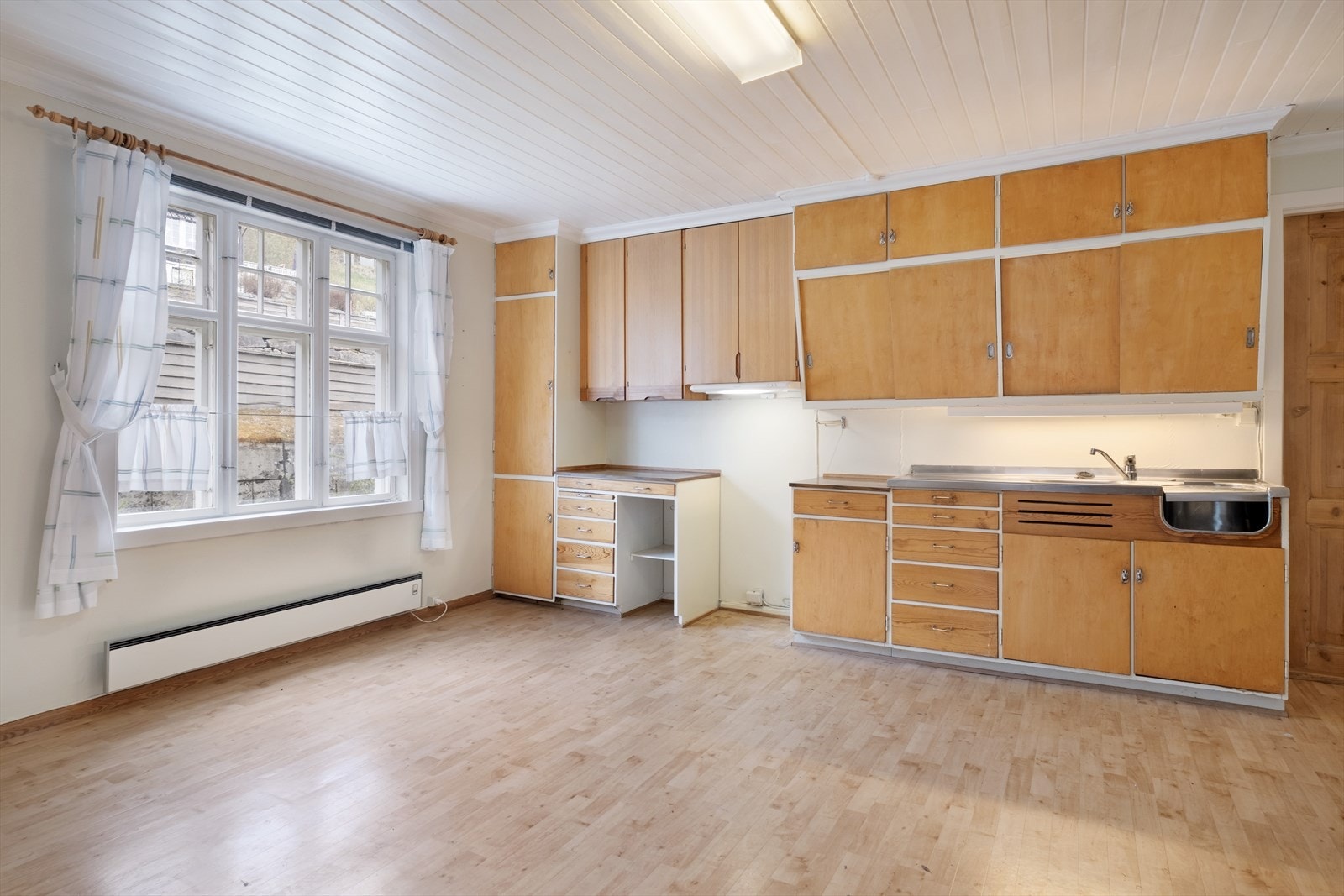 Kjøkken av god storleik med belegg på golv, måla plater på veggane og måla panel i taket. God plass til innreiing av kjøkkenbord. Galleribilde