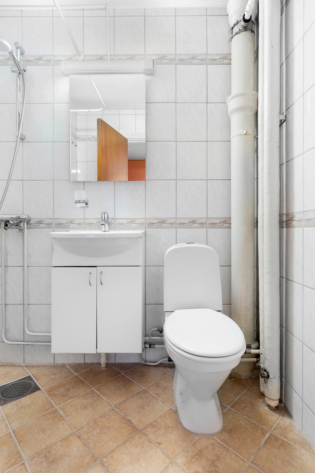 Flislagt bad med varmekabler i gulv. Innredningen består av dusjarmatur på vegg, servant med underskap, gulvstående toalett og opplegg for vaskemaskin. Galleribilde