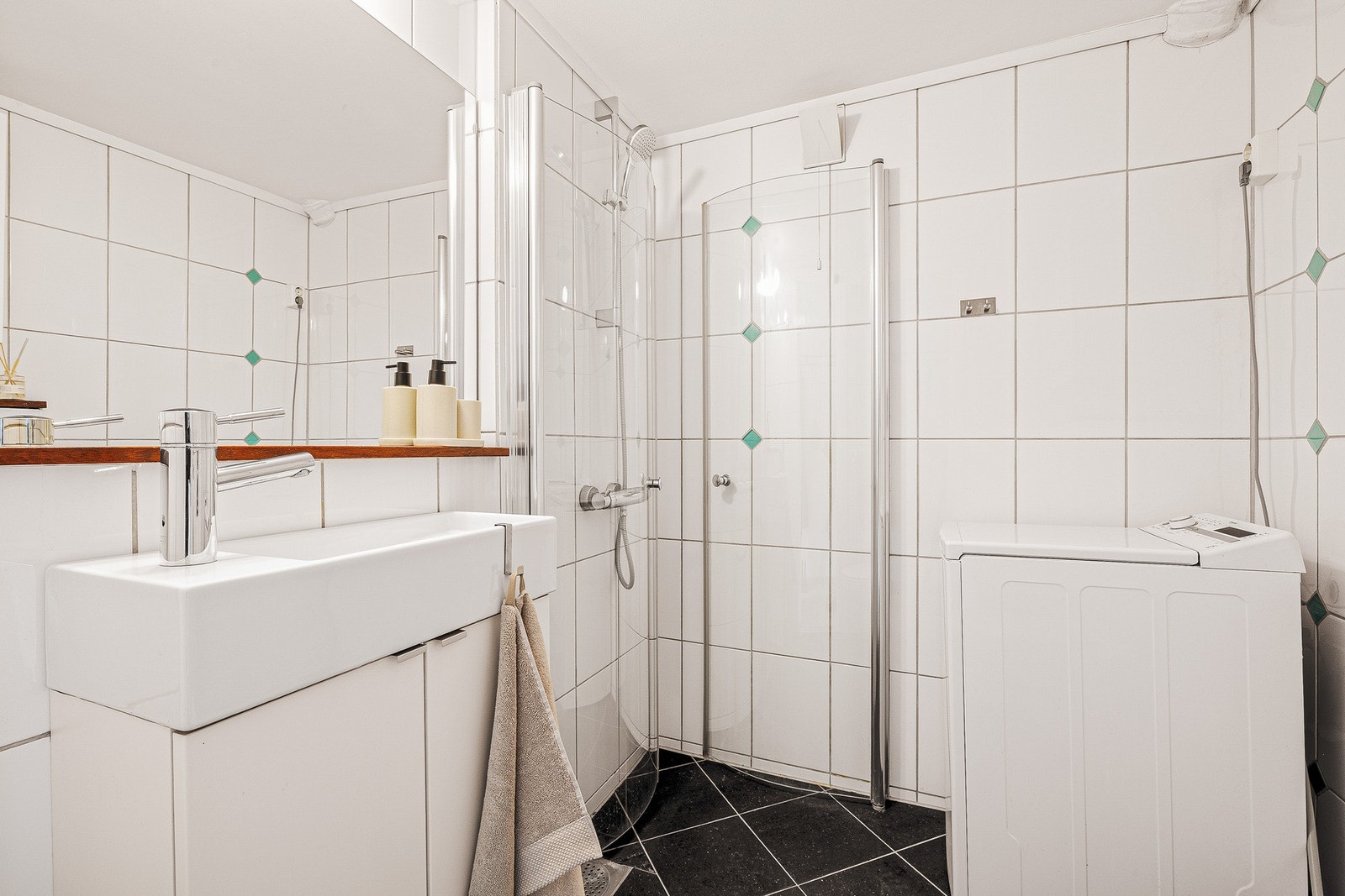Badet er innredet med vegghengt toalett, baderomsinnredning med nedfelt servant, dusjhjørne og opplegg for vaskemaskin. Galleribilde