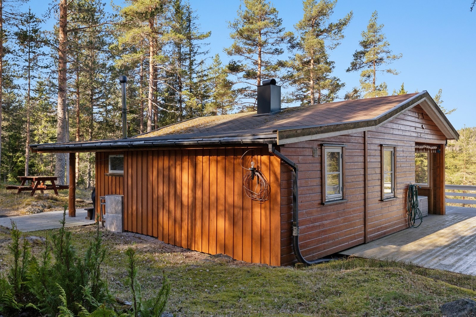 Hytta glir naturlig inn i det omkringliggende skogsterrenget. Bygningens utforming og fargevalg harmonerer med skogens karakter og bidrar til at hytta oppleves som en integrert del av landskapet. Galleribilde