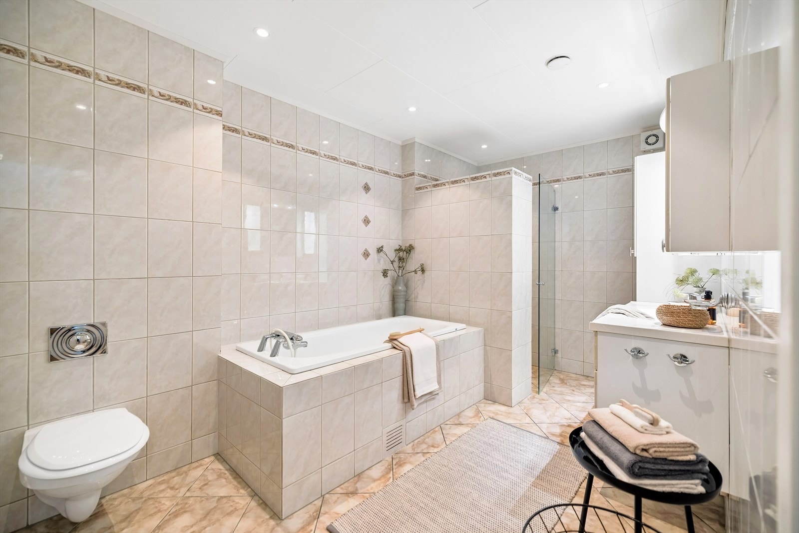 Flislagt bad fra 2002 med gulvvarme, vegghengt toalett og innbygget badekar. Badet er utstyrt med downlights i taket, og nye LED-spotter ble installert i 2024. Galleribilde