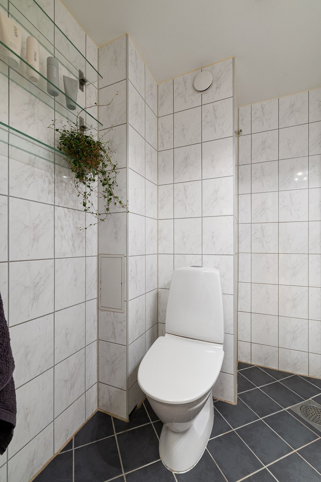 Badet er utstyrt med gulvstående toalett, dusjhjørne med innfellbar glassdør og baderomsinnredning med skap, servant med ettgrepsbatteri og vegghengt speilskap med belysning. Galleribilde