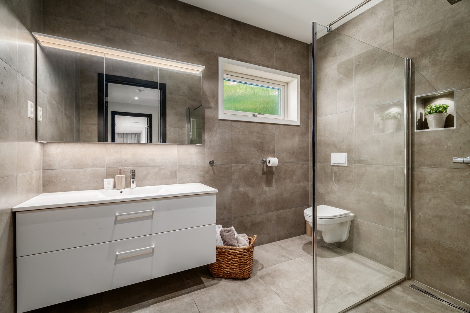 Badet i hovedetasjen er like elegant og har innholdsrik servantinnredning og speilskap, samt vegghengt wc og dusjnisje. Legg merke til den stilrene slukrennen. Galleribilde