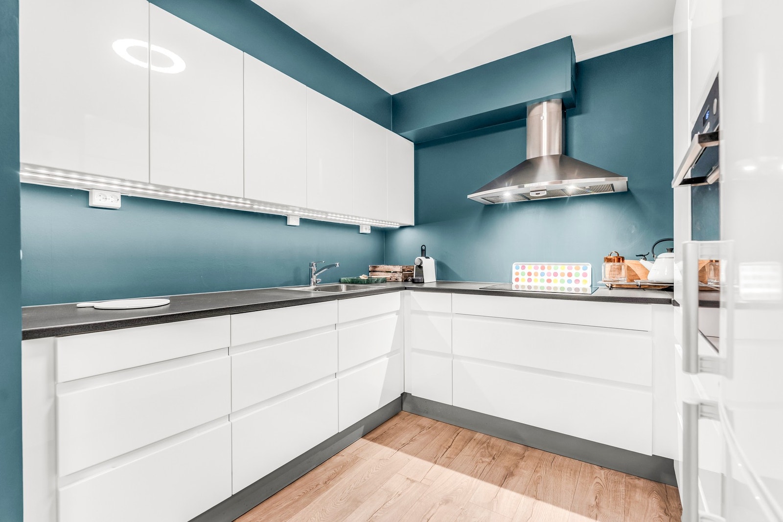 Moderne kjøkken med hvite skapfronter, blå vegger og innebygd ventilator. Galleribilde