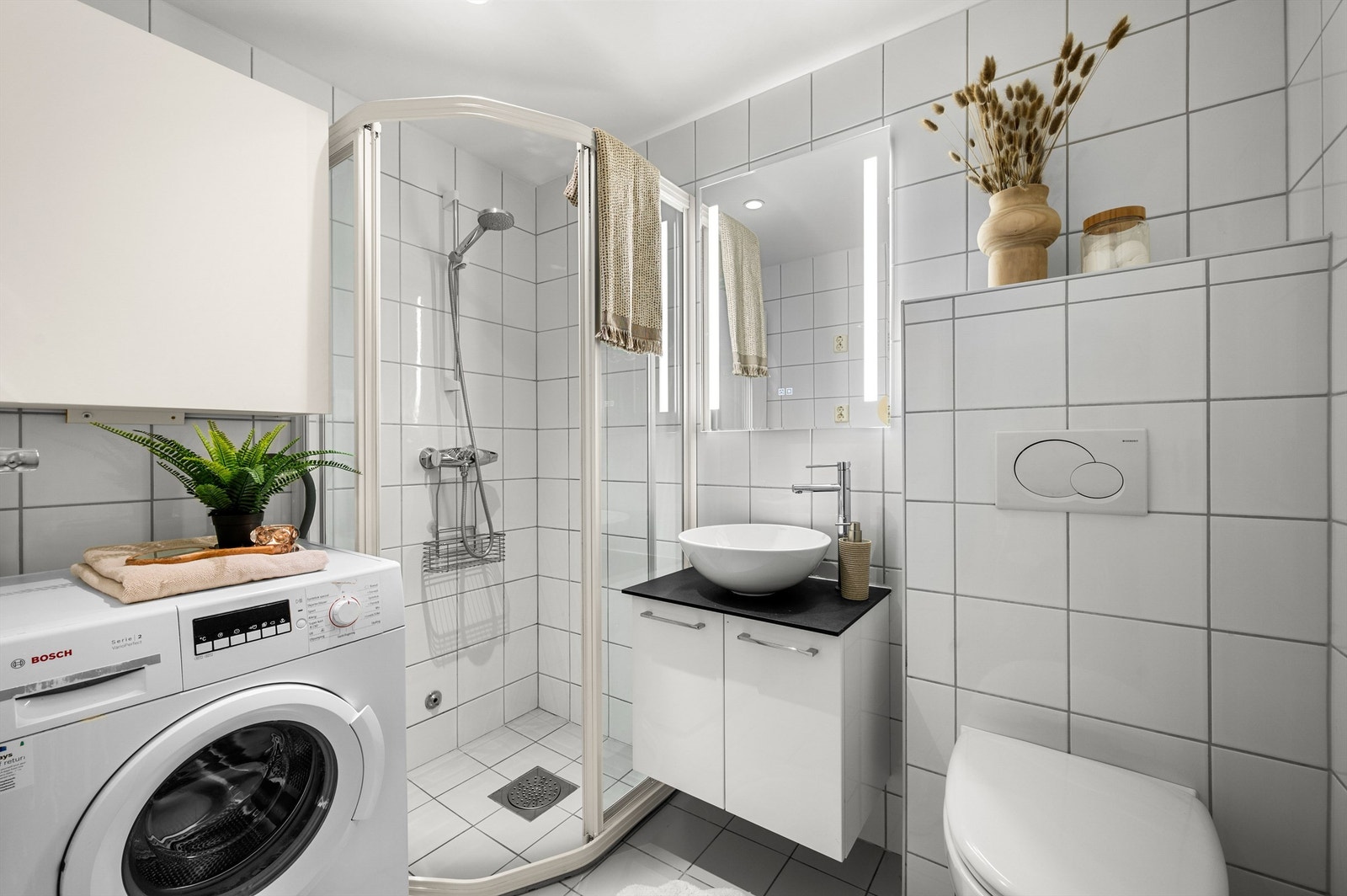 Pent flislagt bad med gulvvarme, downlights i himling og opplegg for vaskemaskin. Videre er badet innredet med servantskap med speil og lys, vegghengt toalett og dusjhjørne. Galleribilde