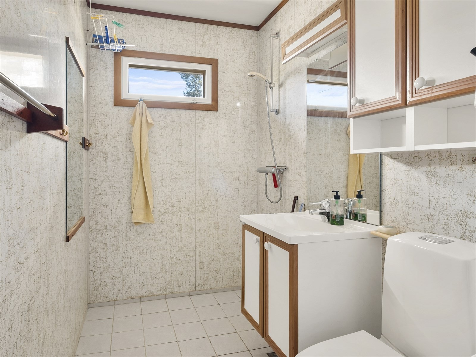 Badet er innredet med servant med oppebvaringshyller, gulvstående toalett, dusjnisje og speil på vegg. Galleribilde