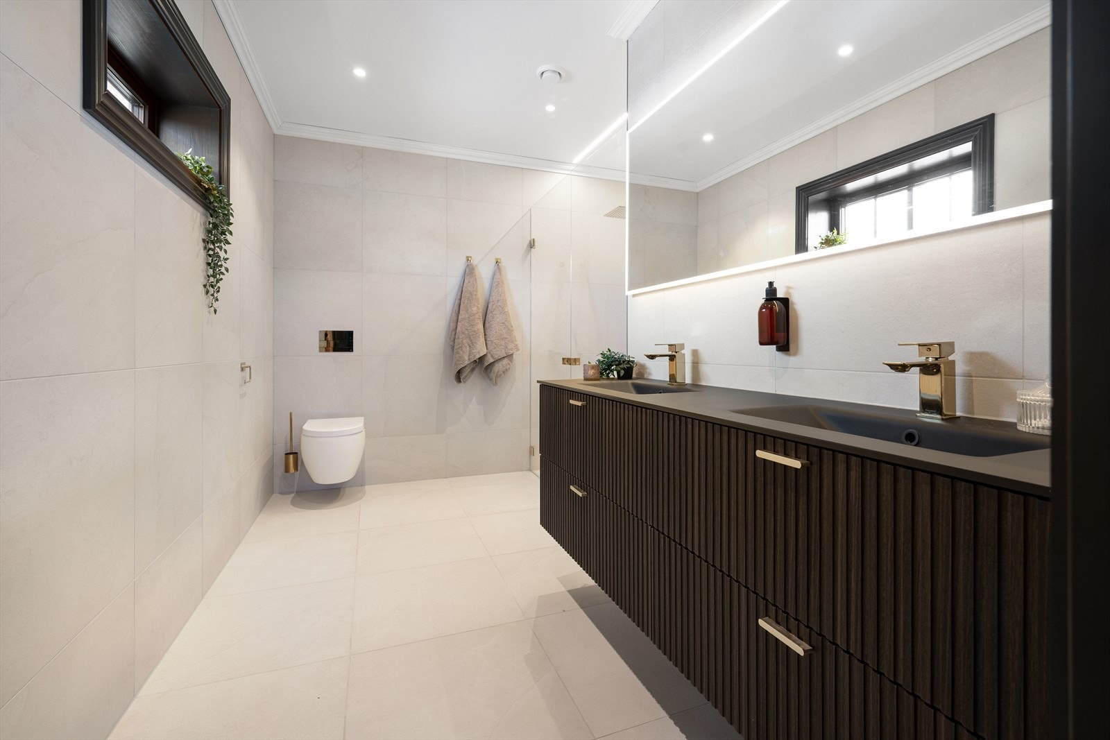Badet tilknyttet soverom 1 er helfliset i lyse, delikate toner og utstyrt med en elegant dobbel servant. Galleribilde