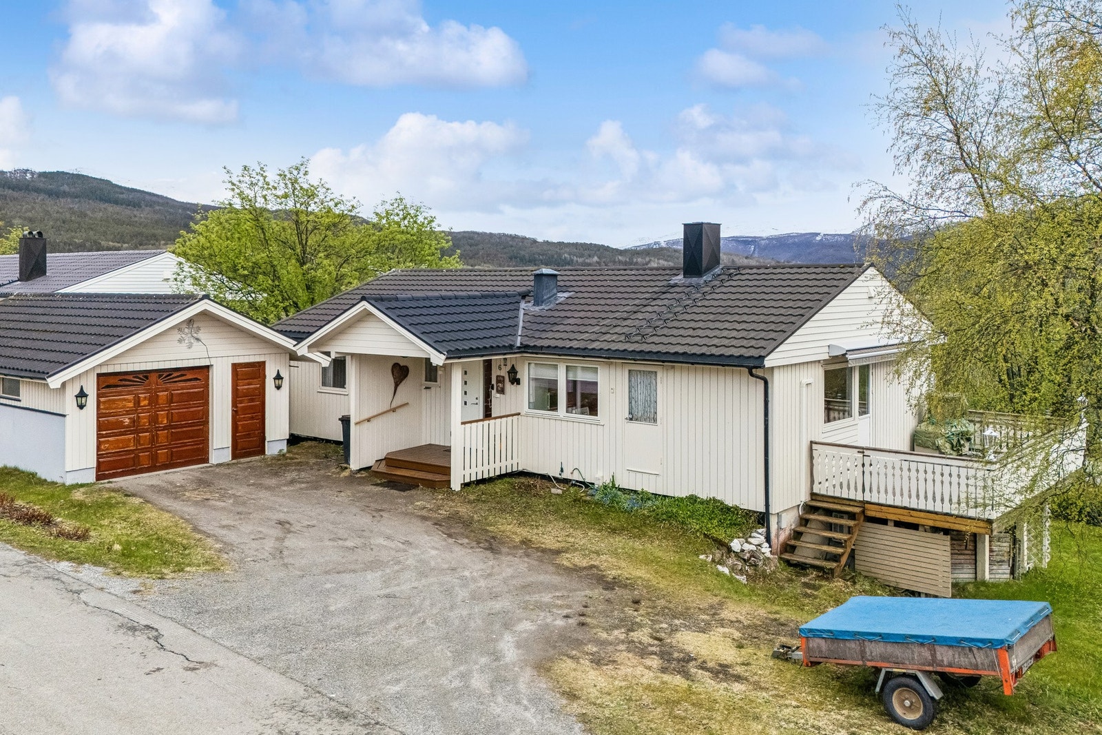 Eiendommen ligger på en skrånende tomt med gruset innkjørsel og en romslig garasje på 34 m² oppført i 1999. Galleribilde