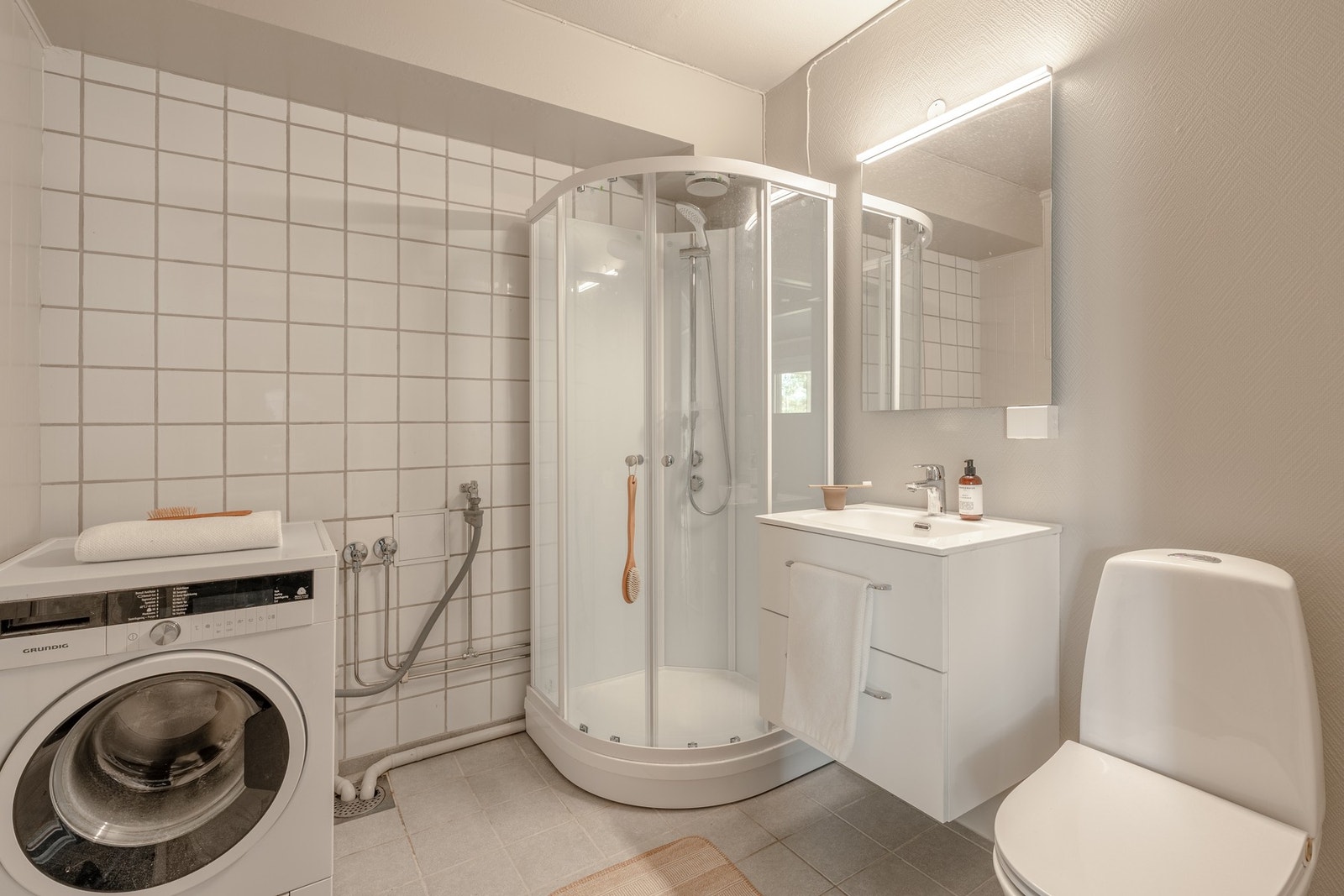 Badet måles til 4,8 kvm. og er fliselagt på gulv, og malt strie på vegg. Her er det opplegg for vaskemaskin og plass til tørketrommel i tårn. Galleribilde