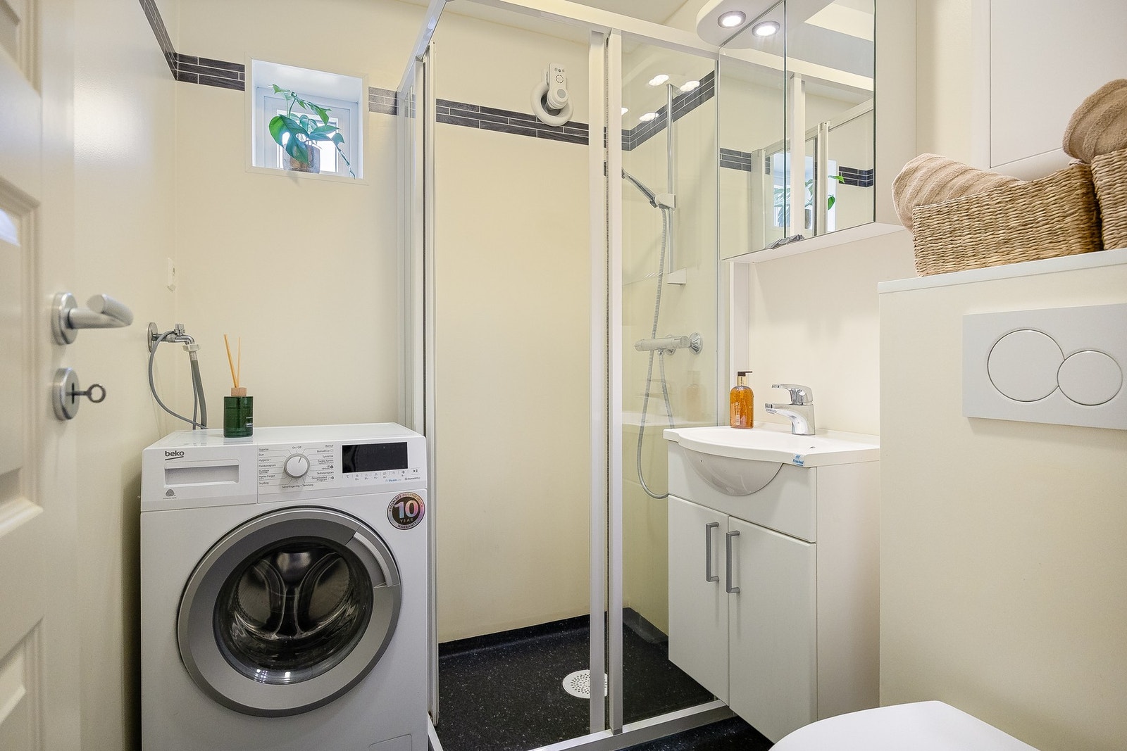 Badet er utstyrt med servant, vegghengt toalett, dusj og opplegg for vaskemaskin Galleribilde