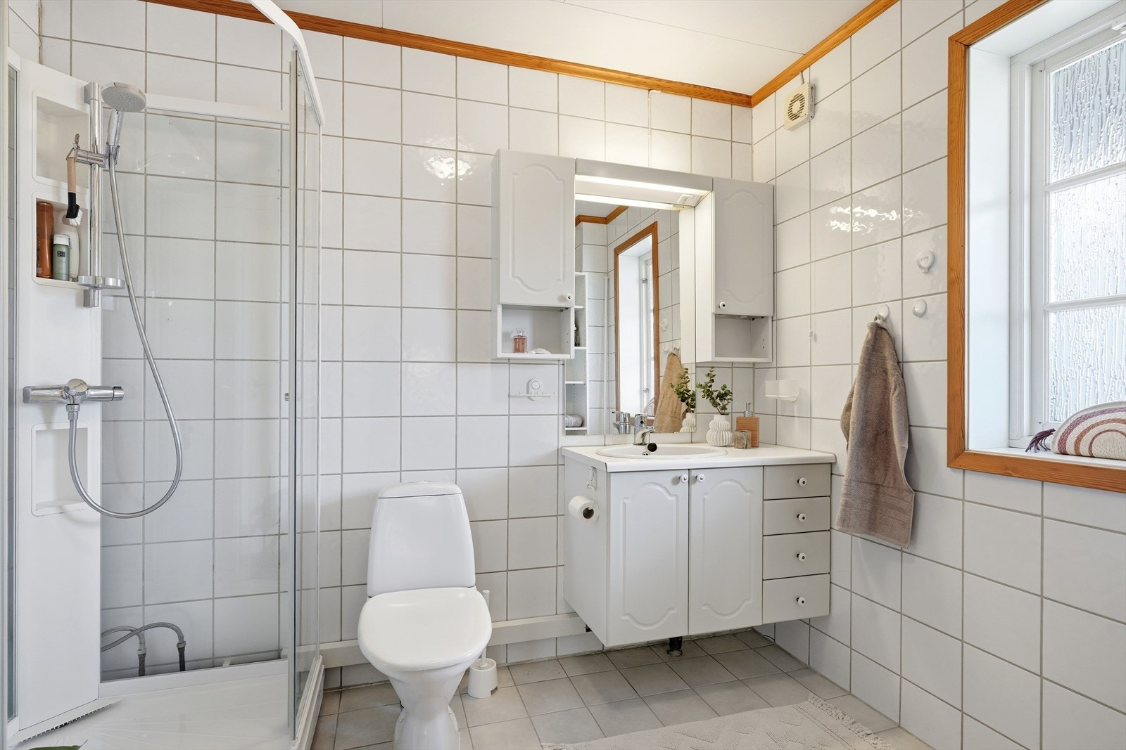 Badet er flislagt og utstyrt med dusjkabinett, toalett og servantinnredning. Galleribilde