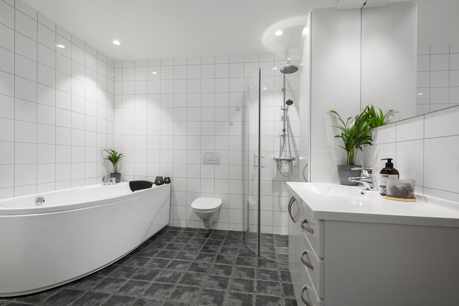 Badet er heilflisa med varmekablar i golvet og downlights i himlinga. Rommet er innreia med dusjhjørne, vegghengt toalett og boblebadekar. Galleribilde
