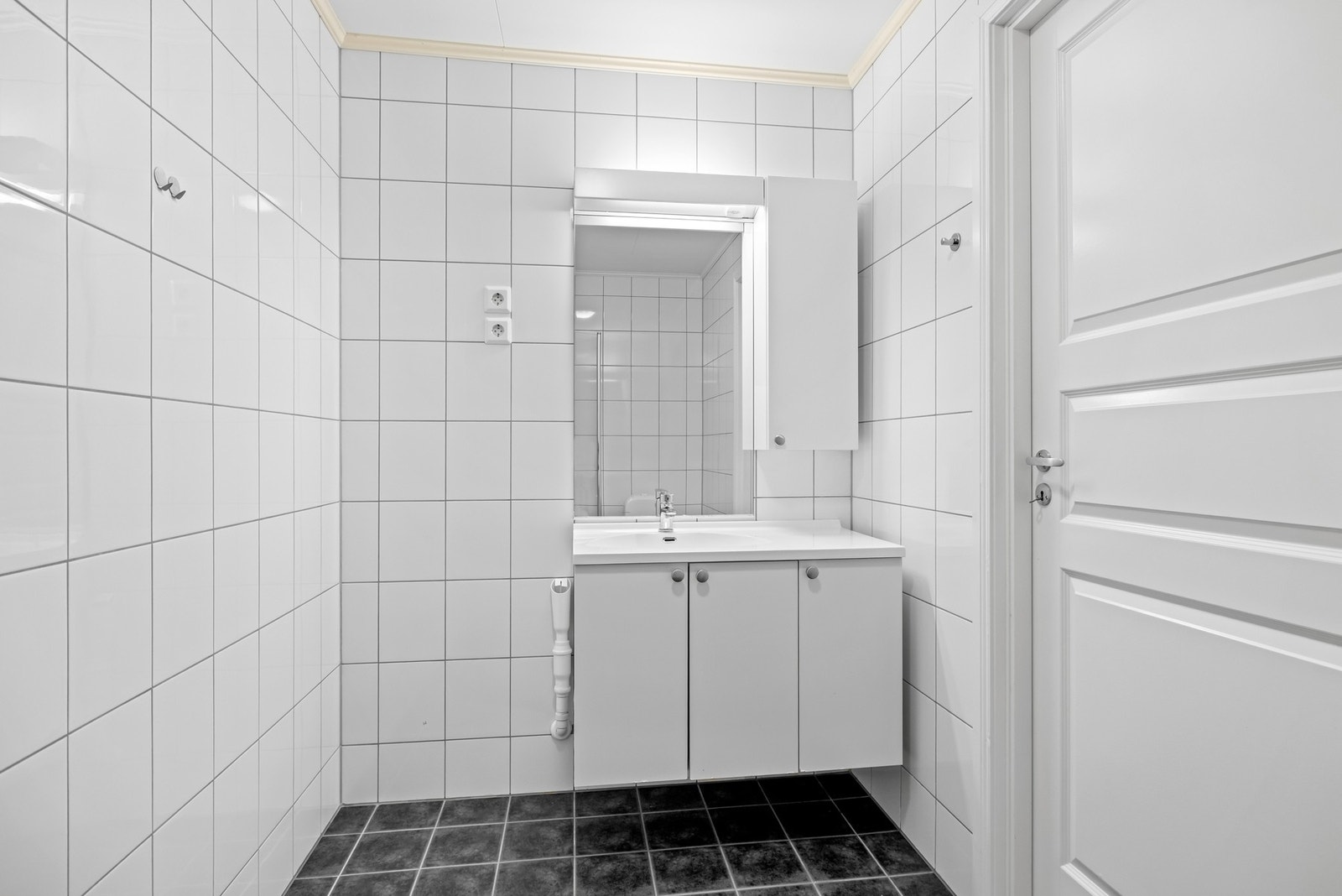 Baderommet har fliser på gulv og vegger og elektrisk gulvvarme. Badet er innredet med en vegghengt innredning med skapdører og overliggende servant med ett-greps armatur. Galleribilde