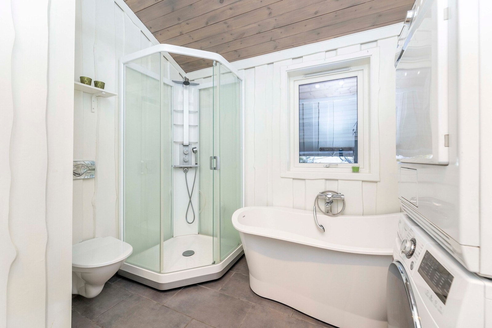 Badet har flislagt gulv med tilhørende sokkel og vegger kledd med malt villmarkspanel, som gir et lunt og helhetlig uttrykk. Galleribilde