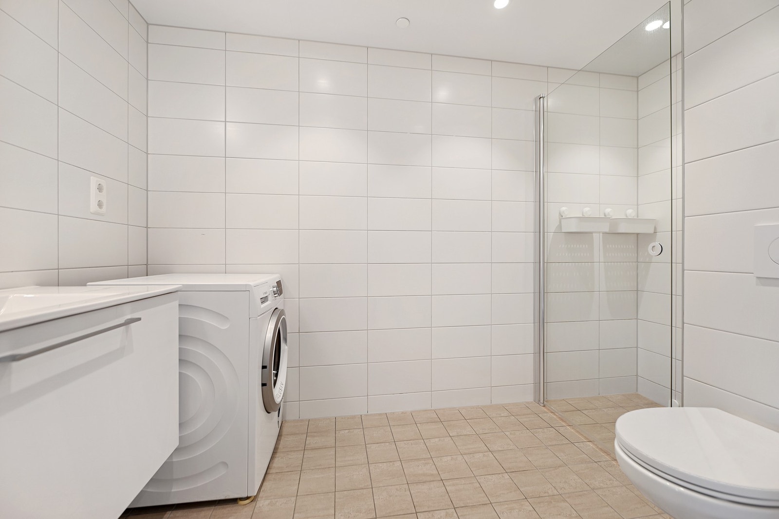 Badet er innredet med nedfelt servant, veggfestet toalett, dusjhjørne og opplegg for vaskemaskin. Galleribilde