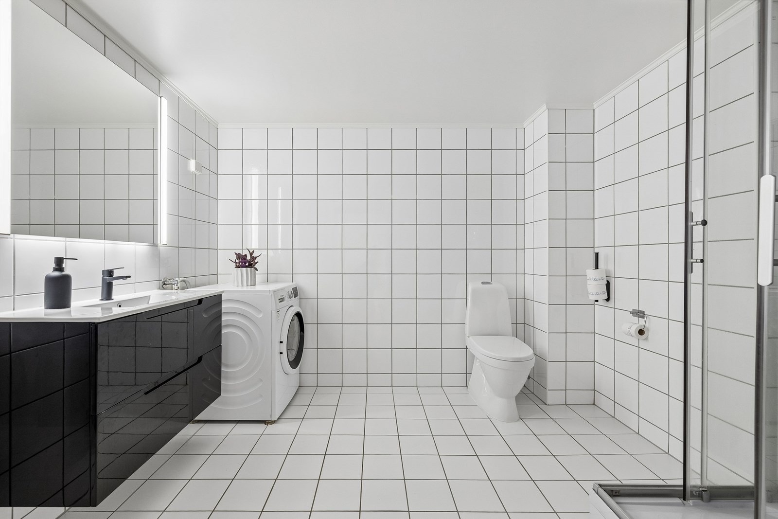 Baderommet er flislagt og har innredning med nedfelt servant, skap, toalett, dusjkabinett og opplegg for vaskemaskin. Galleribilde
