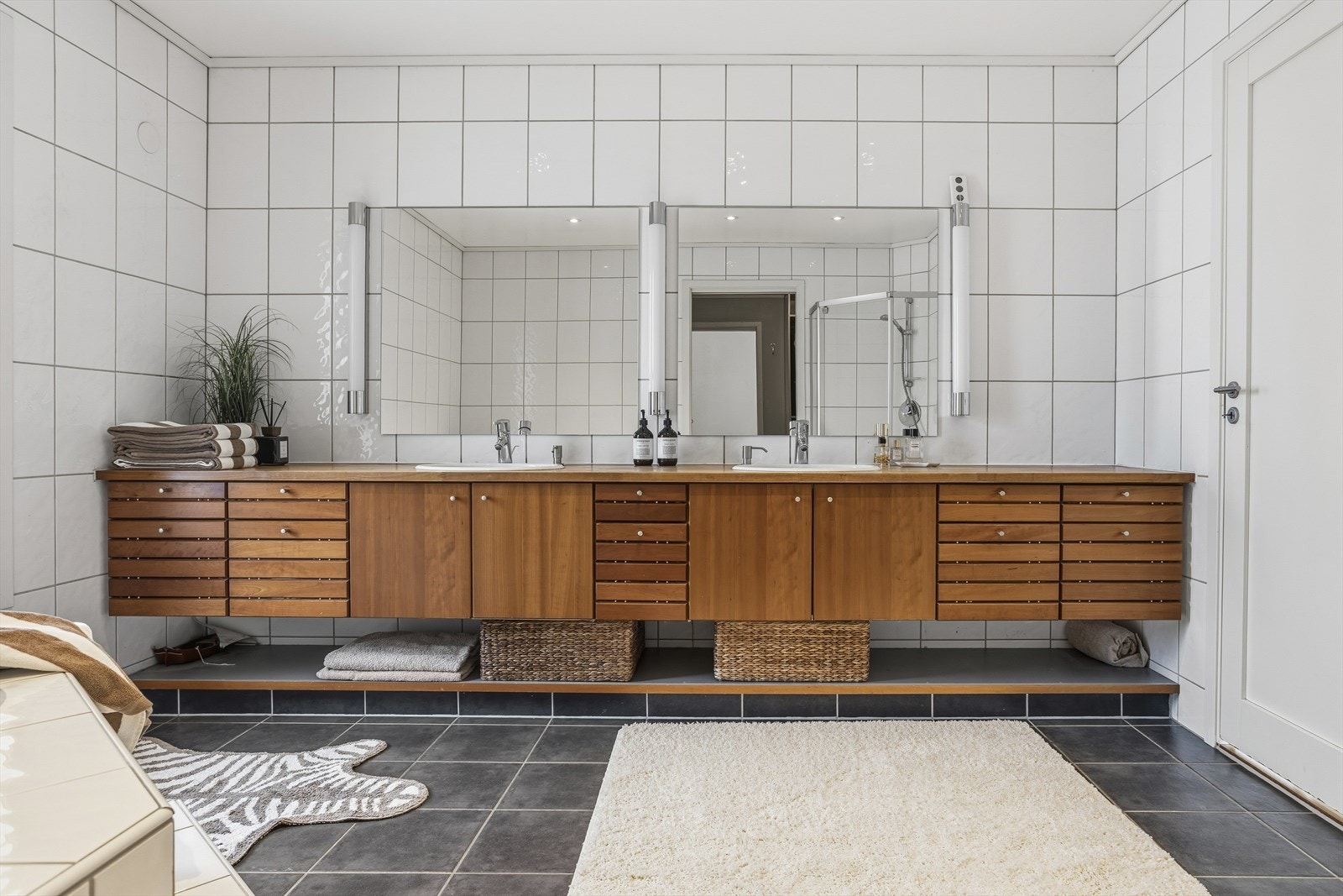 Videre er det direkte tilgang til hovedbadet fra soveromssonen, noe som gir en praktisk og komfortabel løsning i hverdagen. Hovedbadet fremstår som romslig og funksjonelt utformet, med dobbel servant i stilren møbelinnredning i tre. Galleribilde