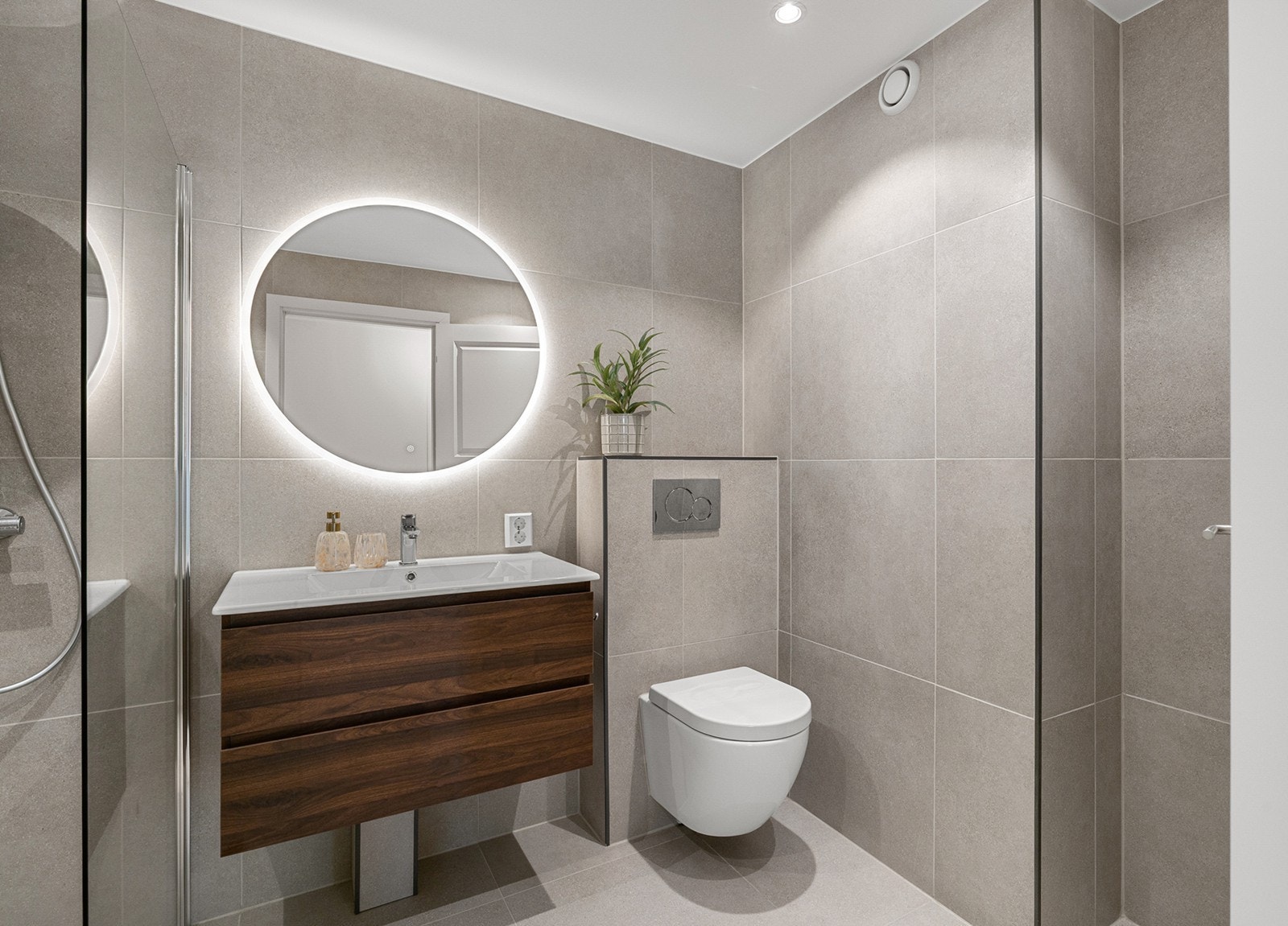 Badet er innredet med stilren baderomsinnredning bestående av underskap, servant og rundt speil med integrert belysning. Galleribilde