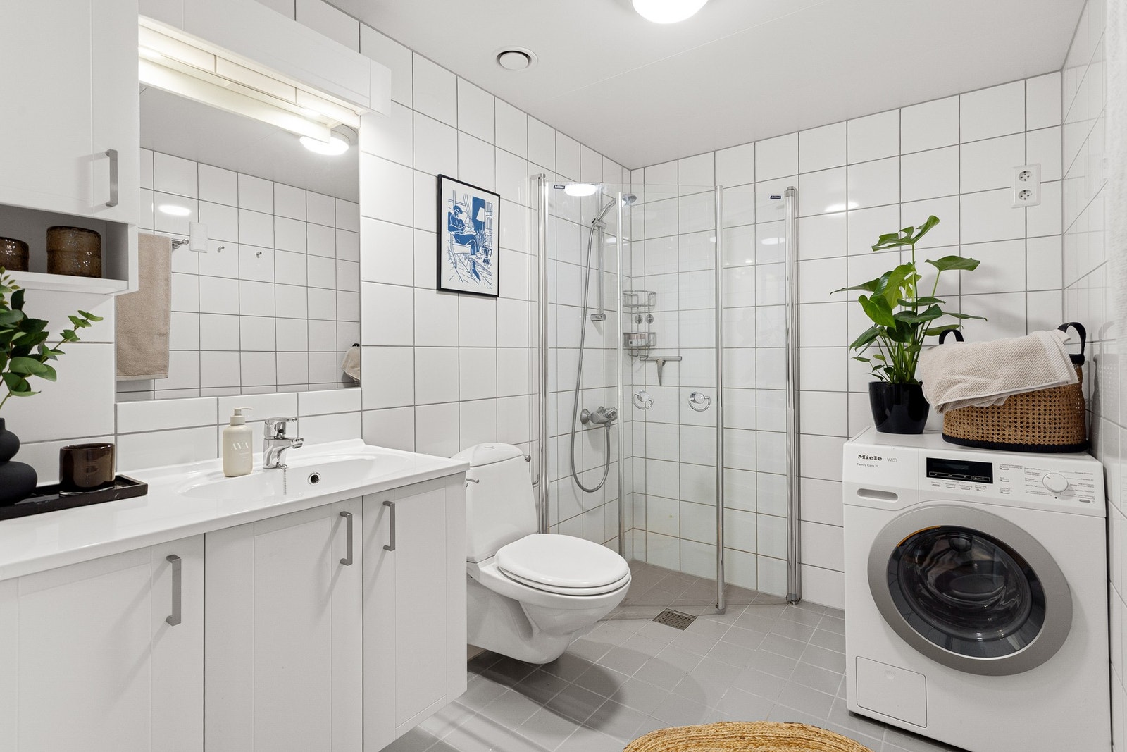 Boligen har et lyst bad med inngang fra entréen. Badet er bygget opp med hvite fliser på vegg og grå fliser på gulv med gulvvarme. Galleribilde
