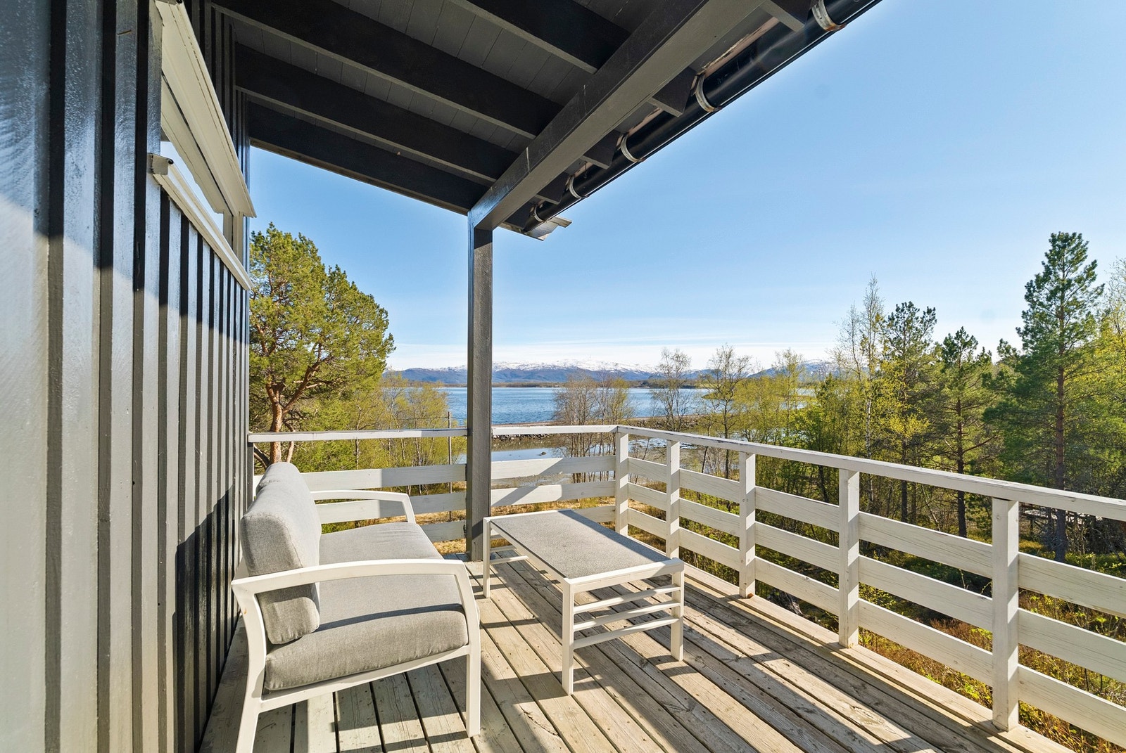 Overbygd balkong med plass til en sittegruppe og utsikt mot sjøen og fjell. Galleribilde