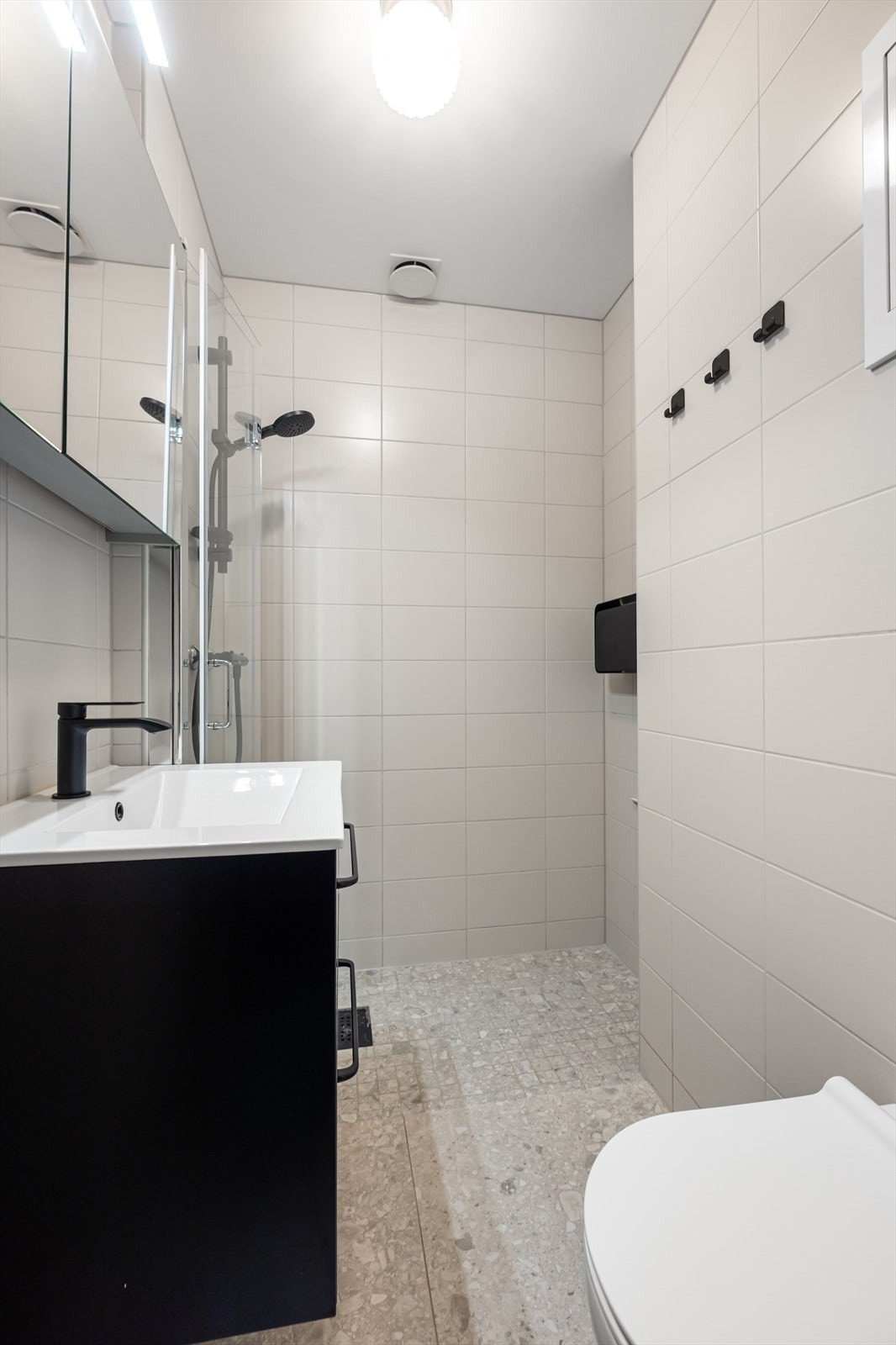 Delikat bad (2022) med fliser på gulv og vegger. Badet er innredet med vegghengt toalett, servant i skuffeinnredning, speilskap og dusj med innfellbare dusjvegger. Galleribilde