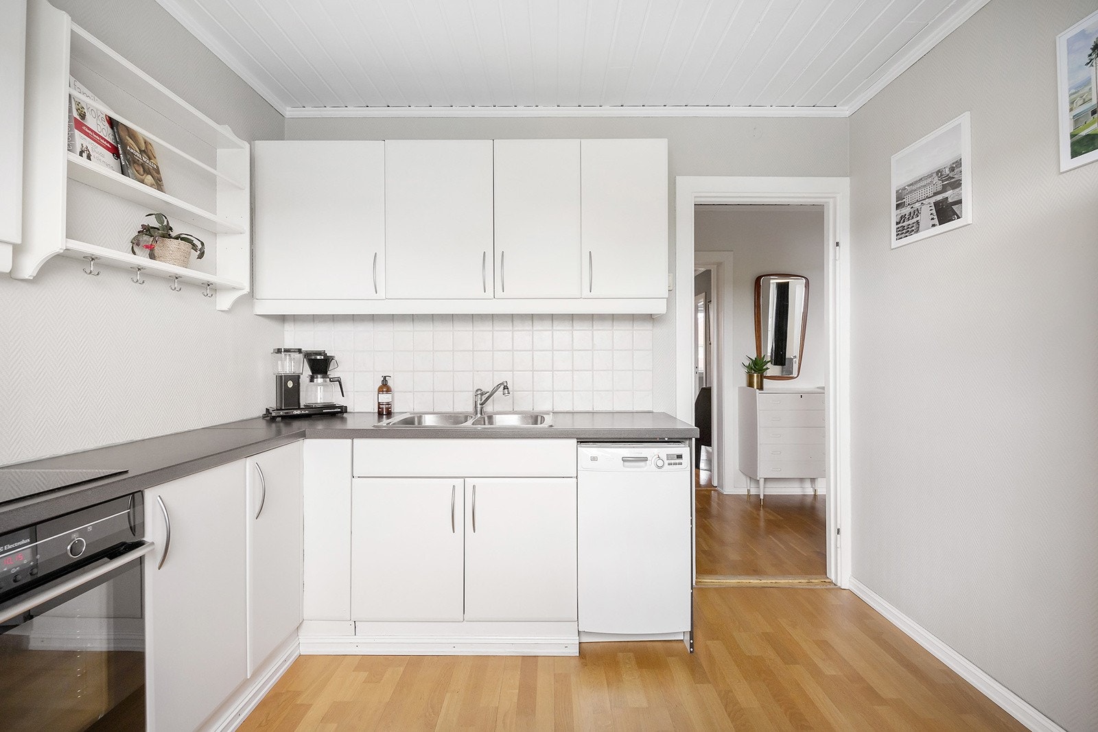 Kjøkken med eldre innredning bestående av glatte, laminerte fronter og laminat benkeplate med fliser over arbeidsbenk. Integrert koketopp og stekeovn, samt frittstående oppvaskmaskin og kjøle-/fryseskap. Dobbel oppvaskkum. Galleribilde