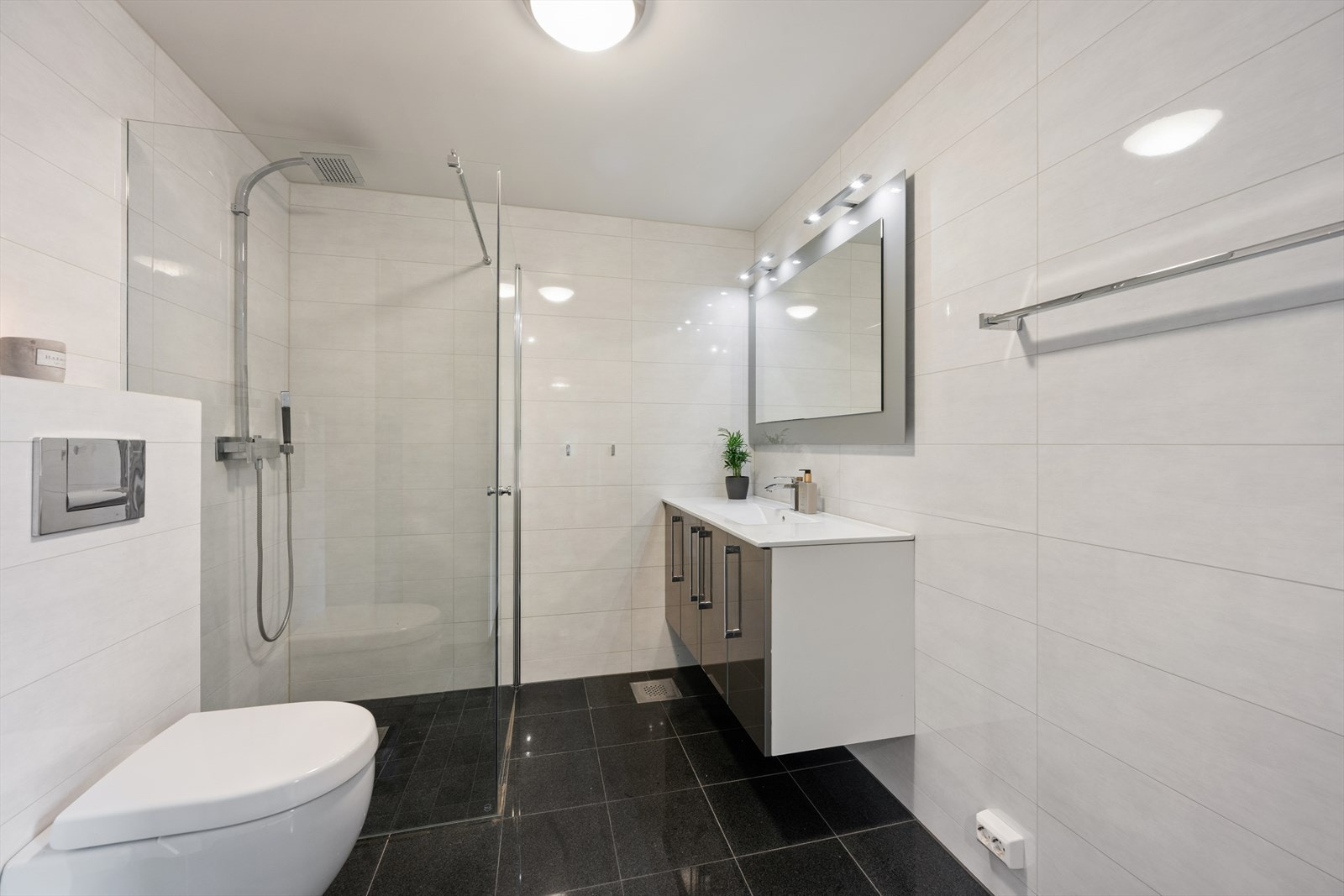 Badet har flislagt gulv, romslig dusjsone, veggmontert toalett og innredning med god lagringsplass. Galleribilde