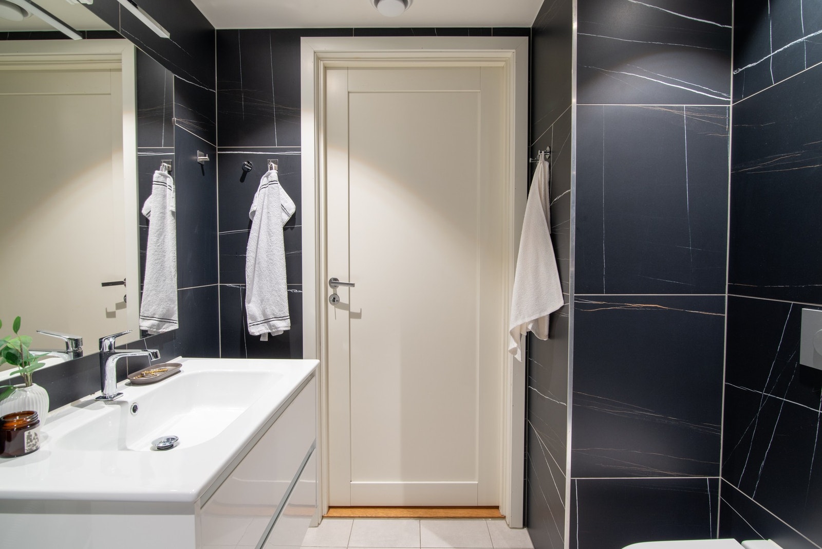 Badet er innredet med romslig dusjhjørne med vegger av glass og dusjgarnityr på vegg, vegghengt toalett, skapinnredning med servant, samt opplegg for vaskemaskin. Galleribilde