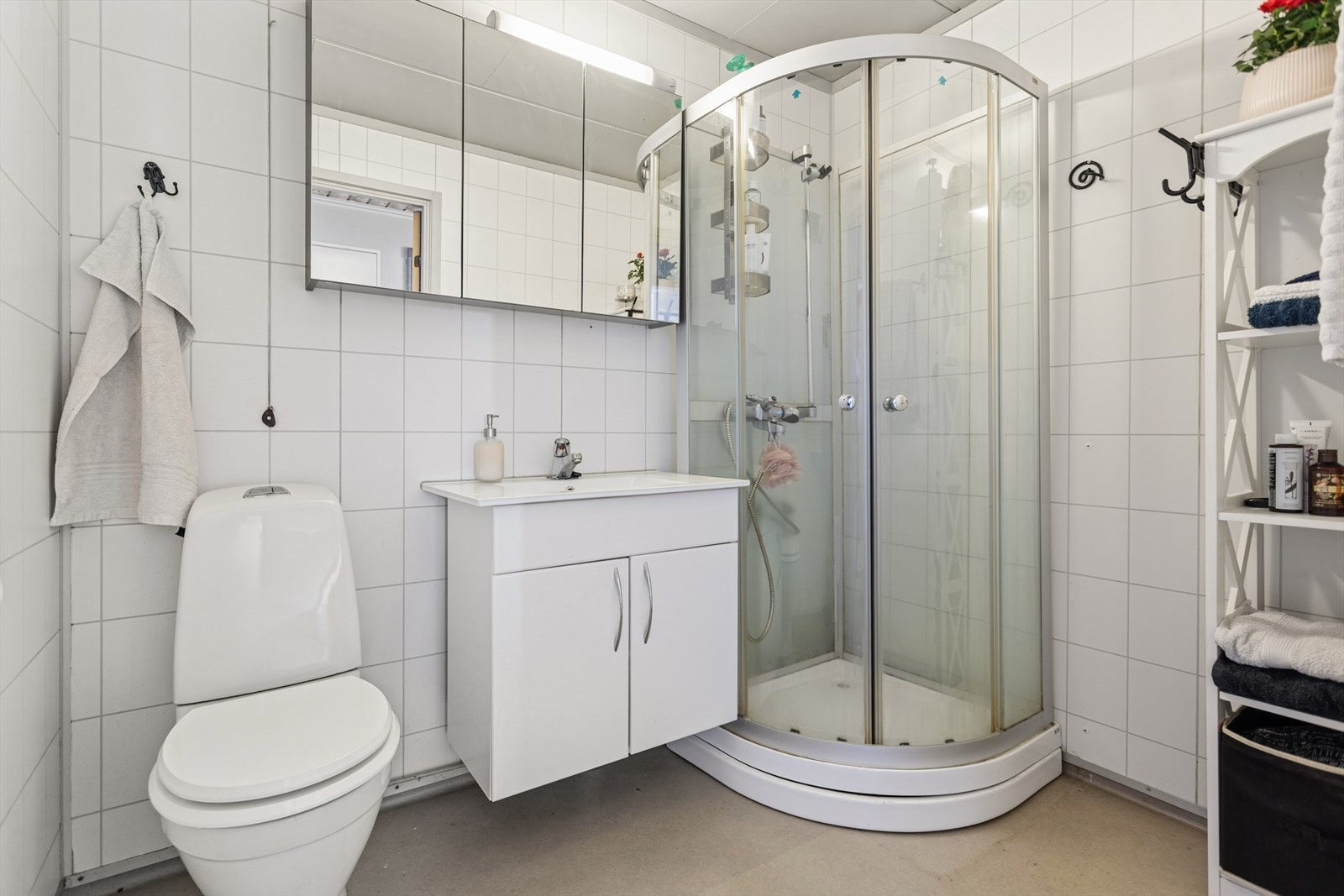 Badet er utstyrt med dusjkabinett, frittstående toalett, samt baderomsinnredning med servant og speilskap. Galleribilde