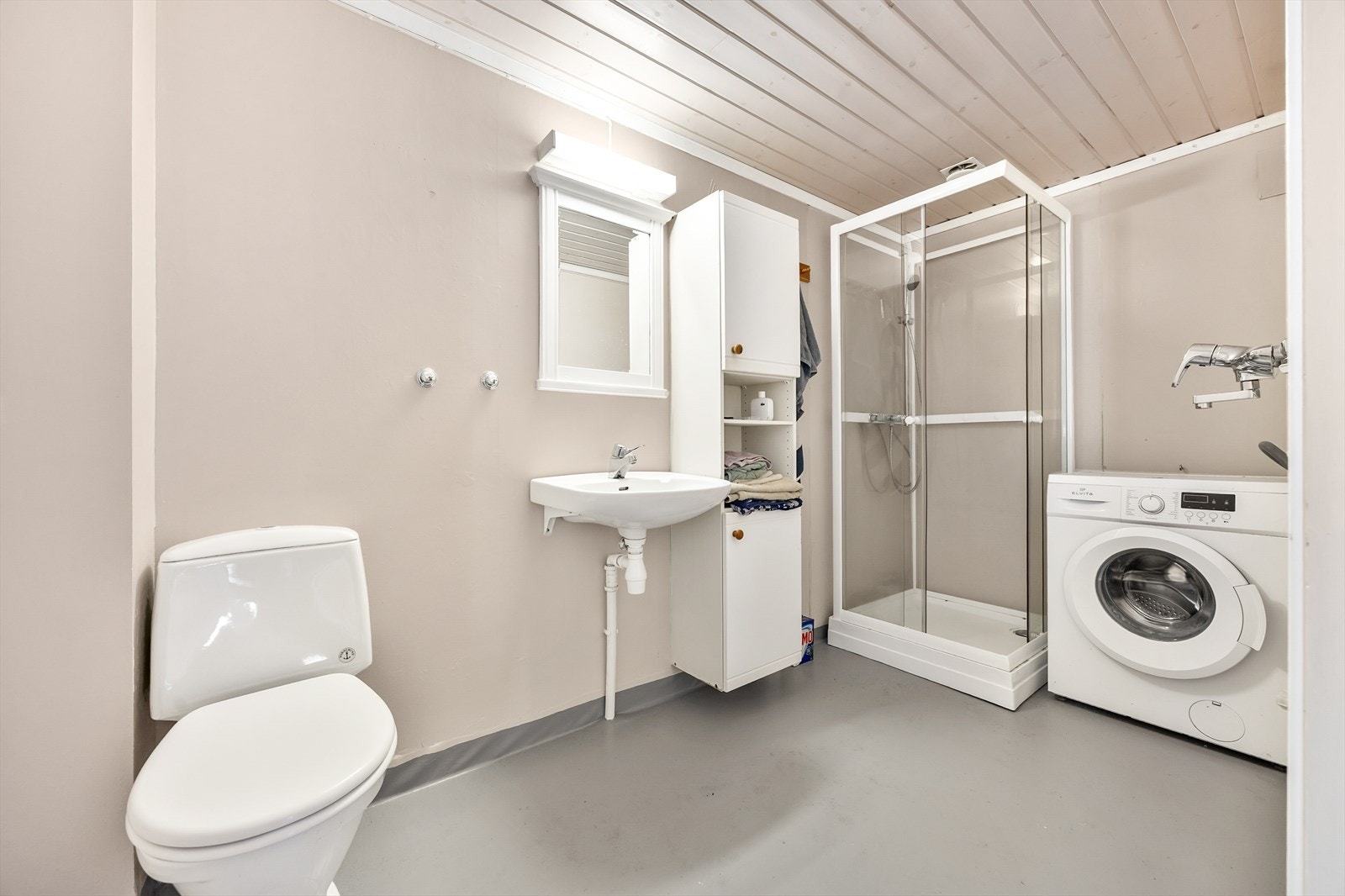 Bad i leilighet b innredet med servant, toalett, vegghengt skap, dusjkabinett og opplegg for vaskemaskin. Galleribilde