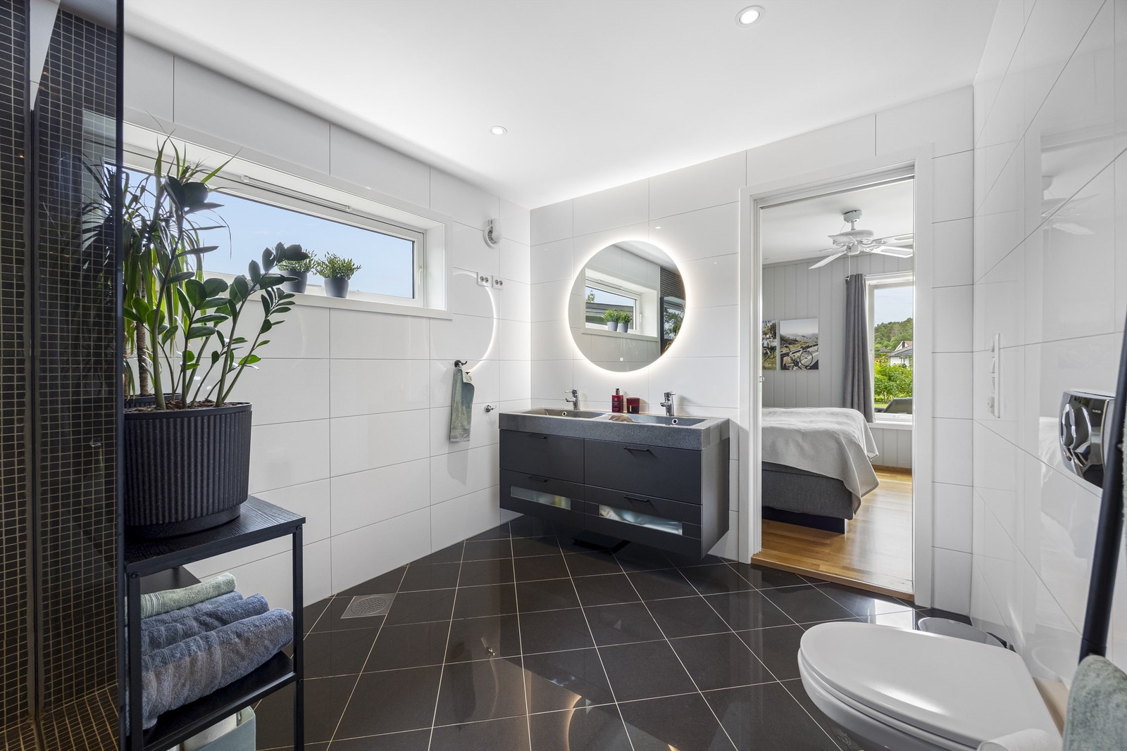 Lekkert bad med adkomst fra soverom og gang. Badet er utstyrt med dobbel servantinnredning, speil med lys, dusjhørne og vegghengt toalett. Galleribilde