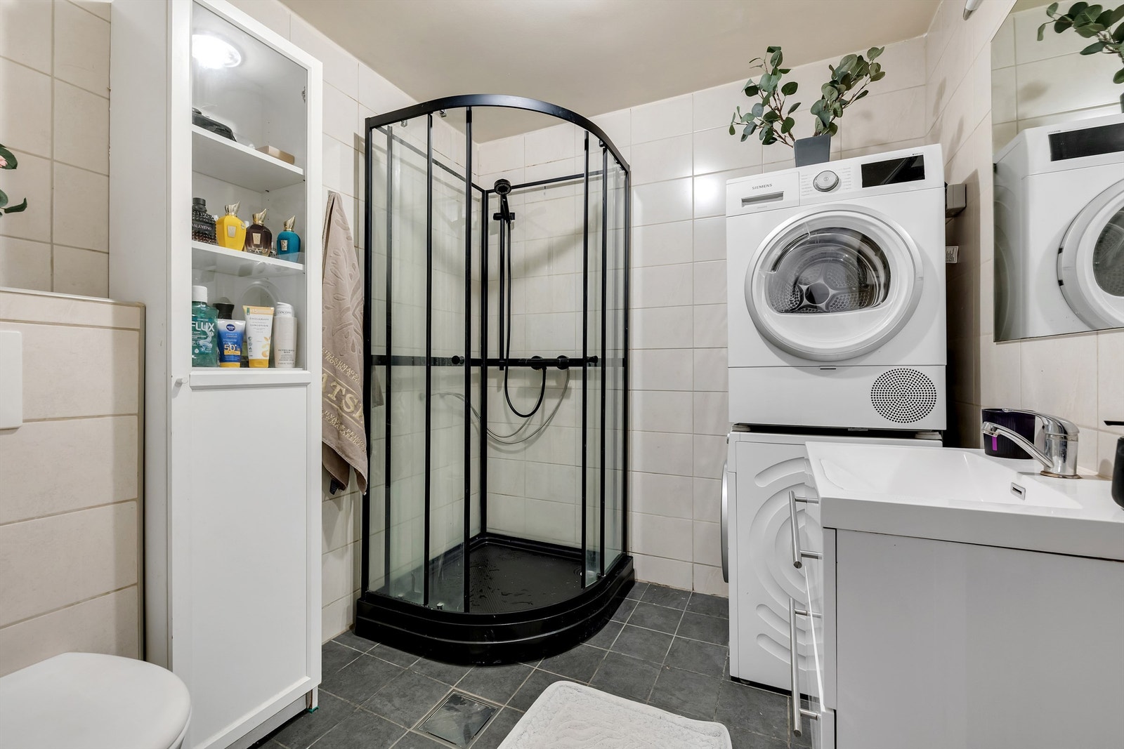Flislagt bad med kabinett, vegghengt klosett, servant med speil og skapløsning, fliser på gulv og vegger. Opplegg for vaskemaskin og tørketrommel. Galleribilde