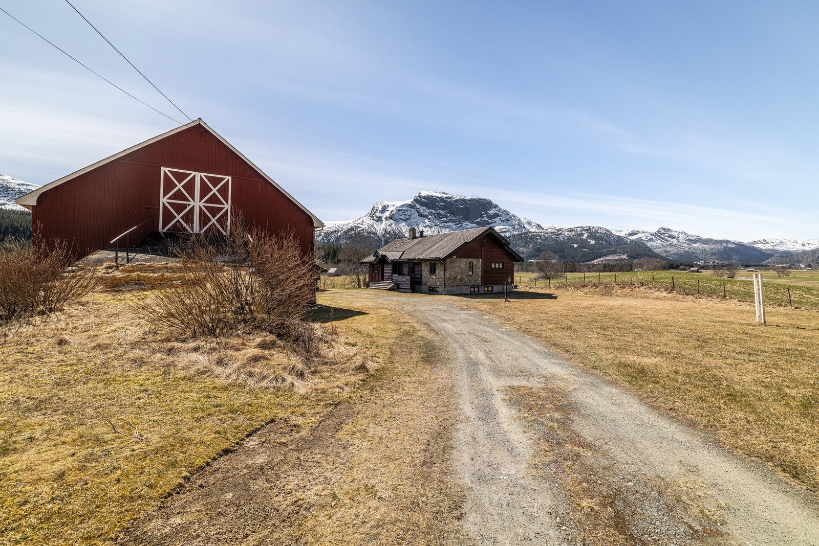 Innkjørsel til tunet med låve til venstre og boligen bakenfor, fjellene som bakteppe. Galleribilde