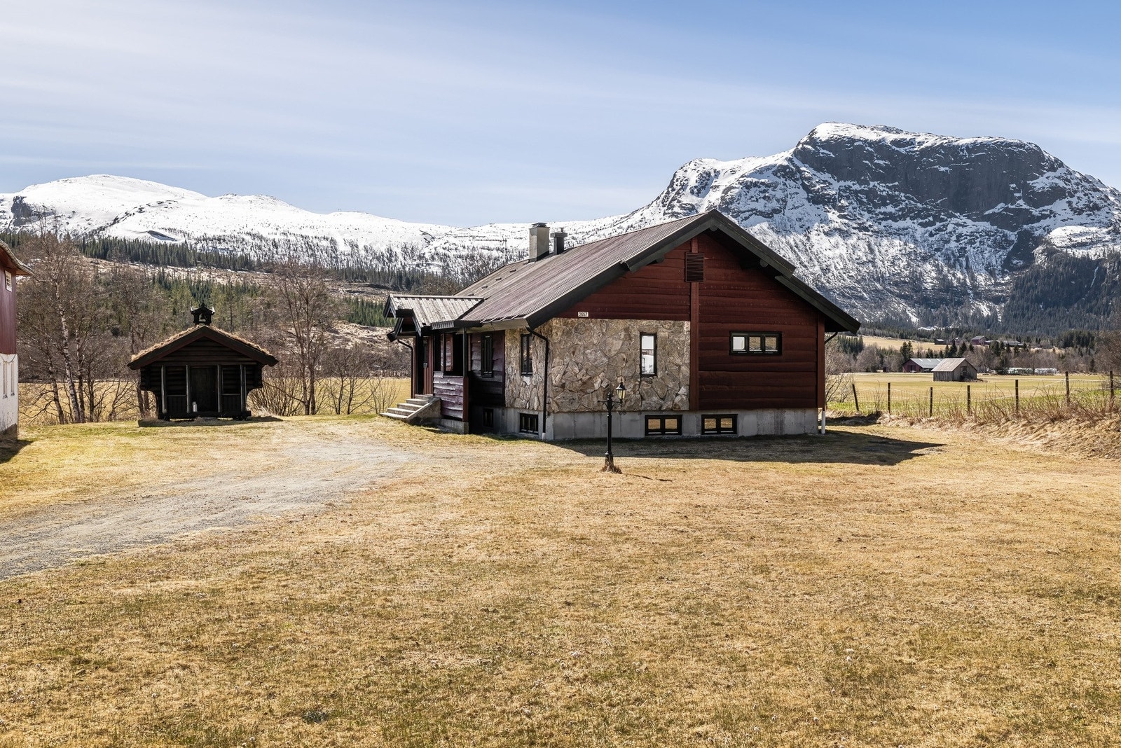 Boligen er kledd med naturstein og rødmalt panel, med stabbur i forgrunnen. Galleribilde