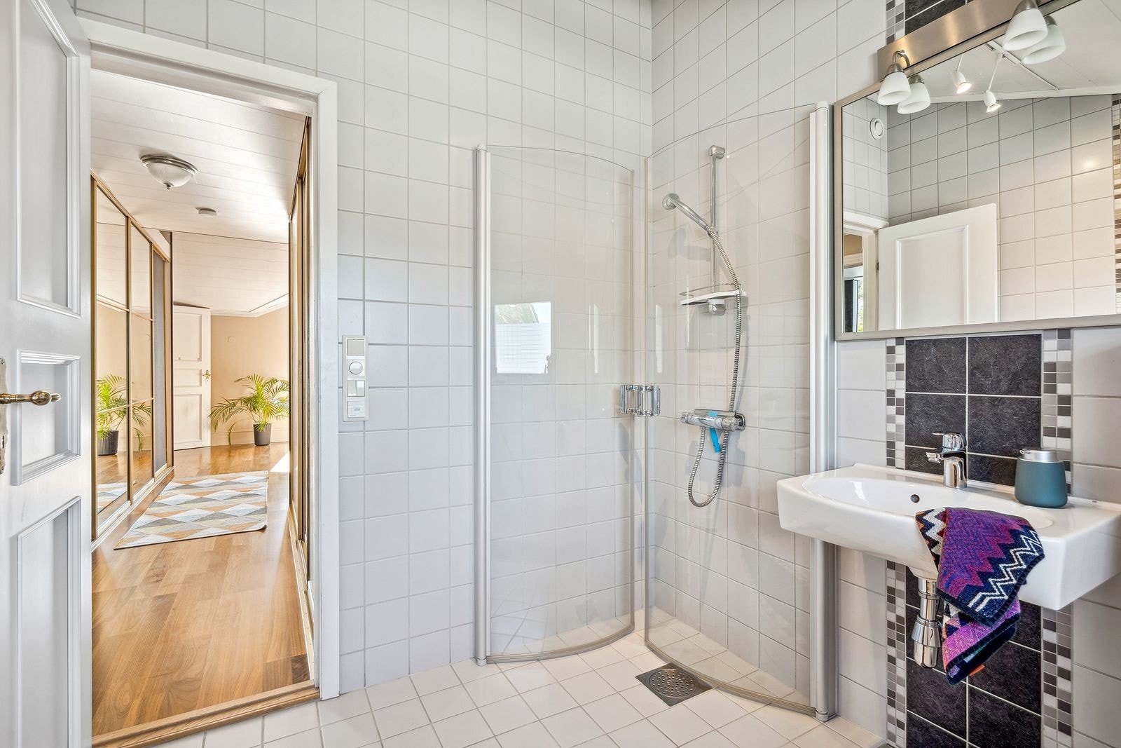 Flislagt bad innredet med servant, speil med belysning, WC og dusjhjørne med innfellbare dører.