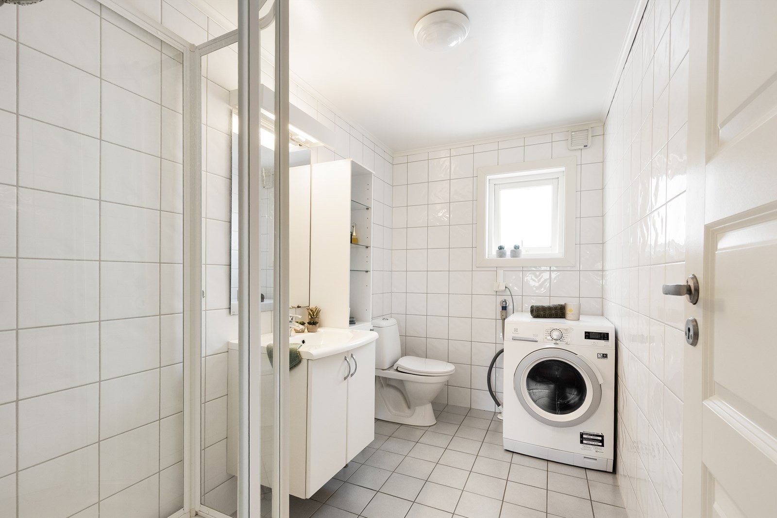 Lyst, flislagt bad med standard fra ca. 2008. Badet er utstyrt med elektriske varmekabler i gulv, gulvmontert toalett, dusjkabinett og opplegg for vaskemaskin. Galleribilde