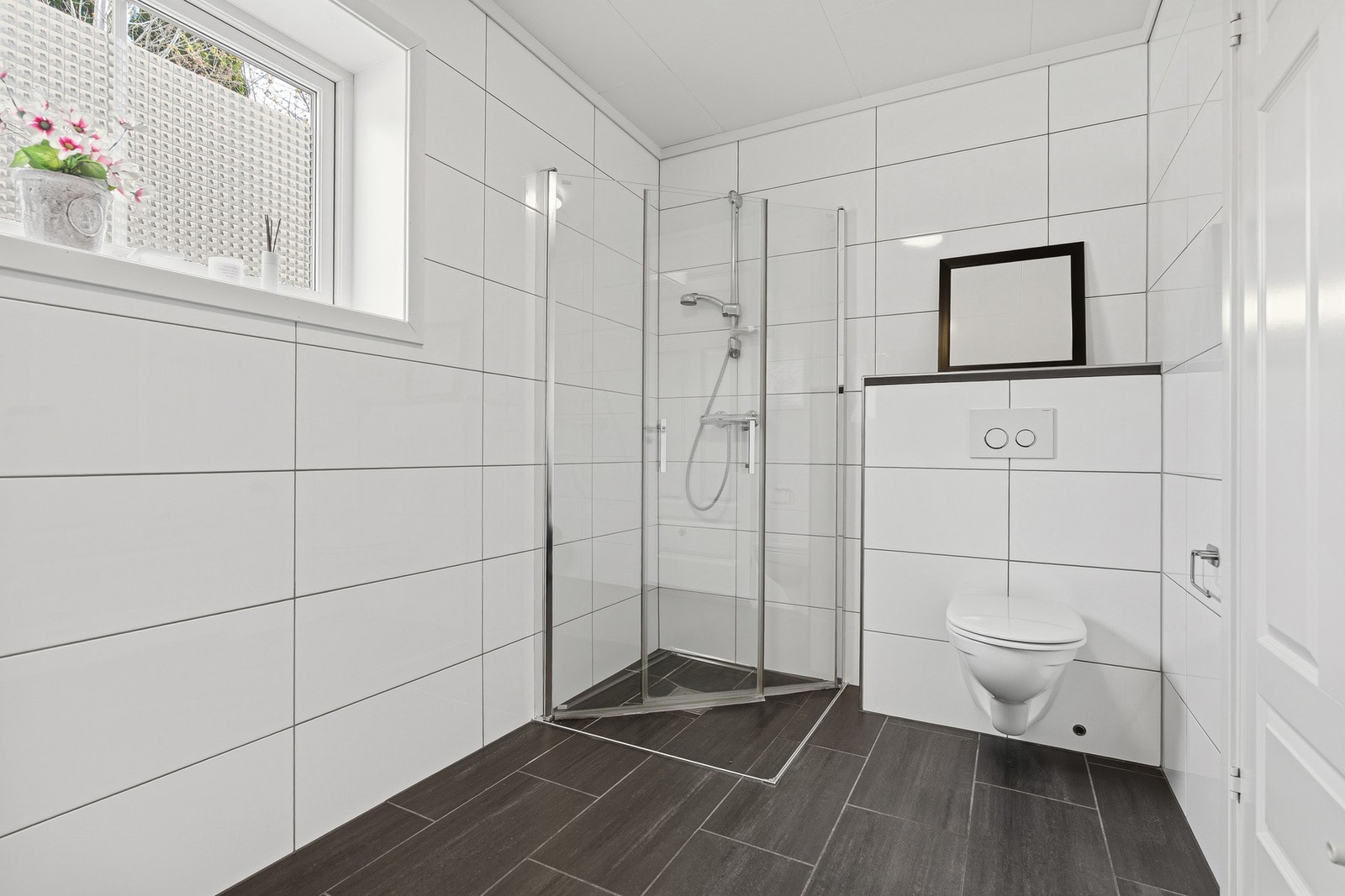 Badet har
stilrene overflater og praktisk dusjløsning med glassvegger, og vegghengt toalett. Vinduet sørger for naturlig lys og en
og behagelig atmosfære. Galleribilde